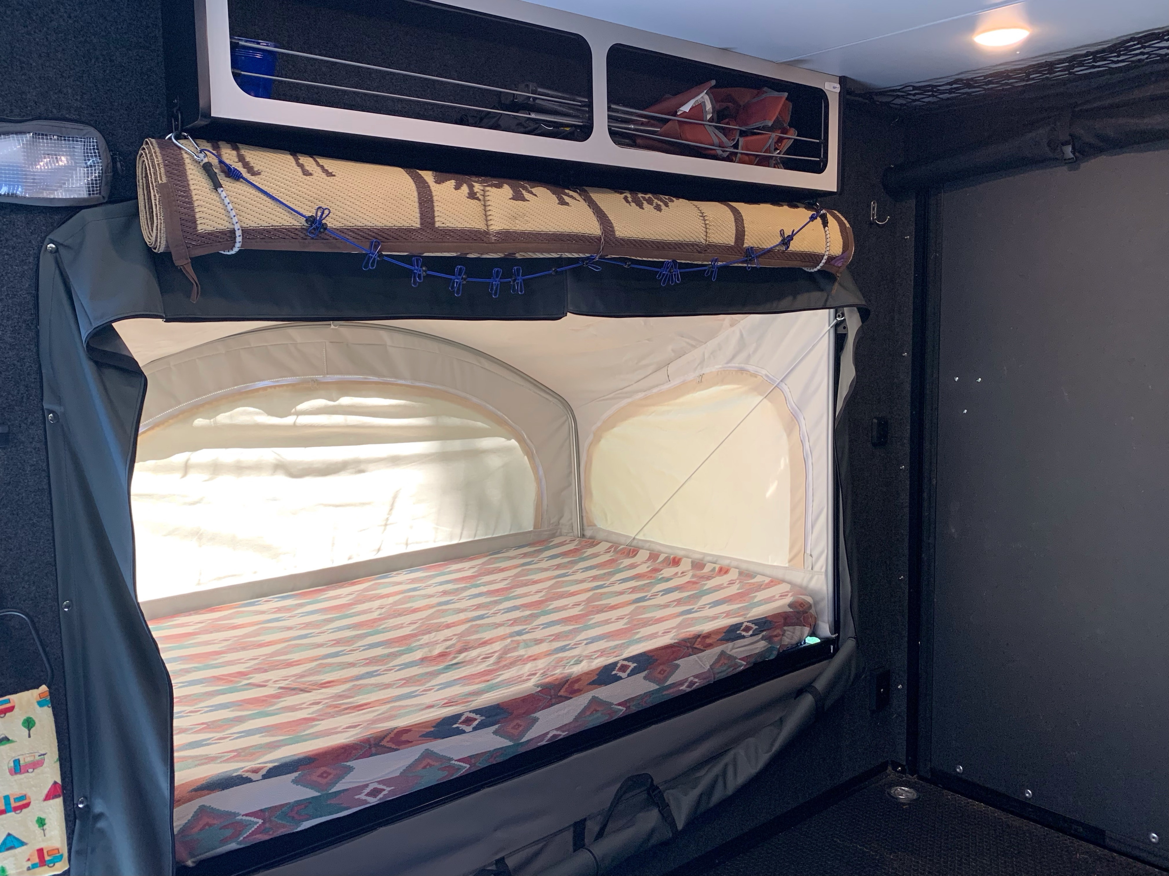 RV rental interior: a pop-up bunk bed with patterned mattress, overhead storage, and a rolled mat, ready for camping adventures.. InTech RV Flyer Discover 2021