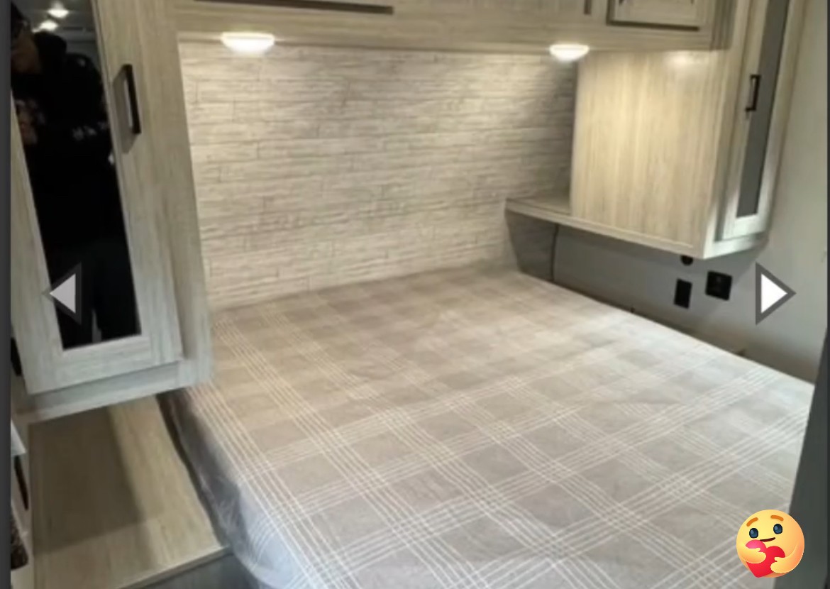 Comfortable RV rental bedroom featuring a plaid bedspread, overhead storage, and an integrated shelf with power outlets.. Coachmen Explore 2026 273DBHCK 2026