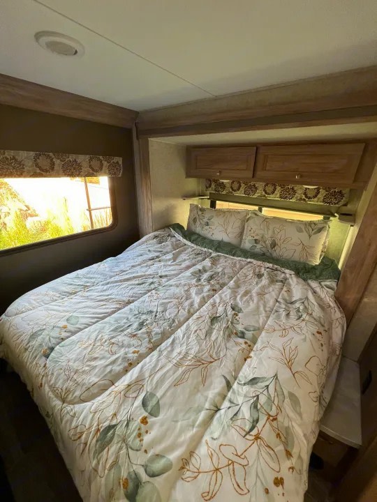 Experience comfort in this RV rental bedroom with a nature-inspired comforter, wooden cabinets, and a scenic window view.. Forester 2251SLE 2020
