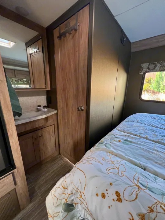 This rv rental interior showcases a cozy bedroom with a floral comforter, alongside a compact bathroom vanity and closet.. Forester 2251SLE 2020