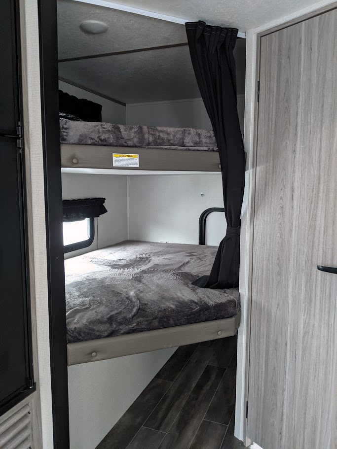 RV rental bunk beds: cozy sleeping area with privacy curtain, ideal for families in a travel trailer.. Keystone RV Passport SL 2021