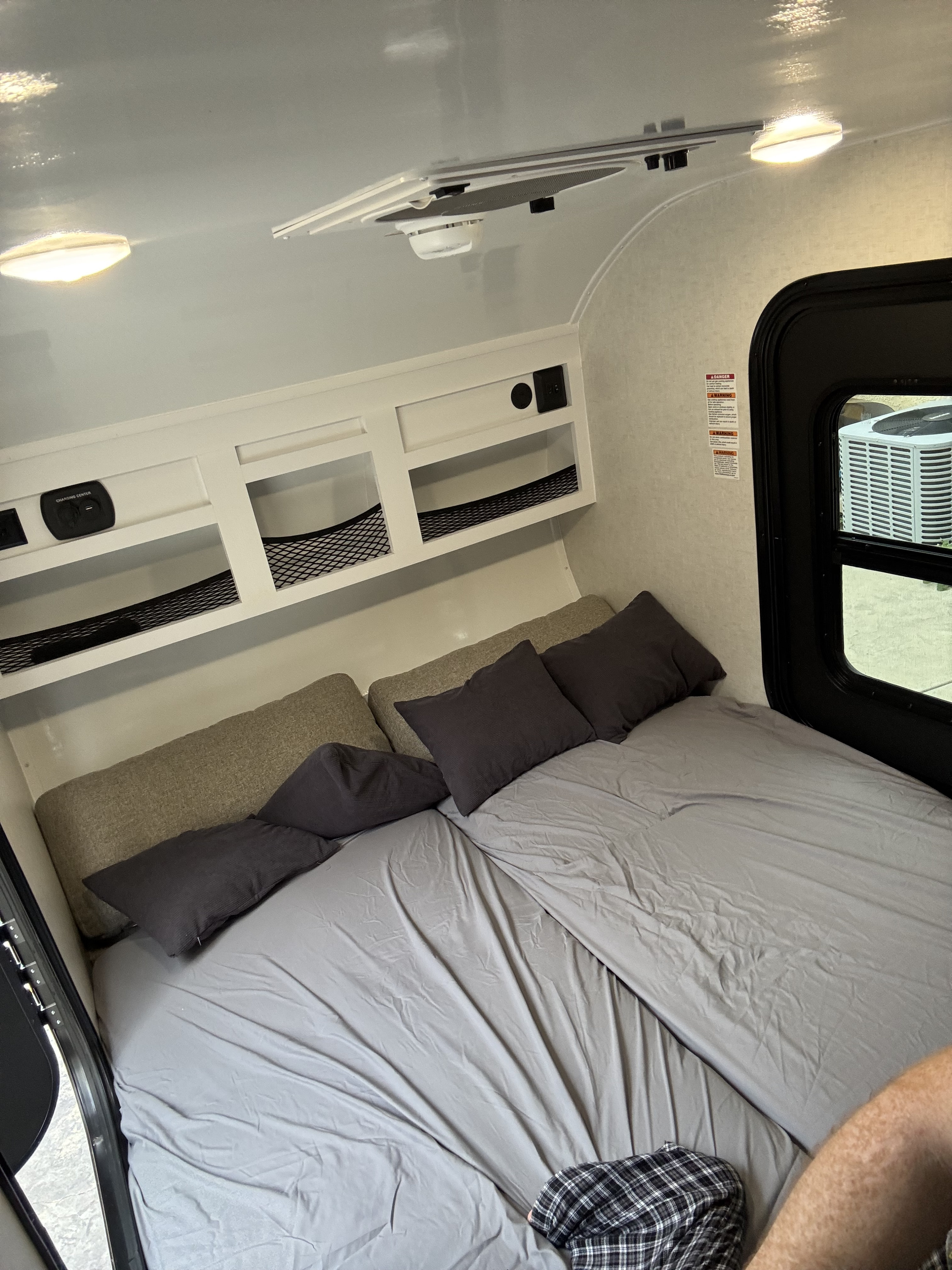 Cozy RV rental interior featuring a bedroom with gray bedding, overhead storage, charging center, ceiling lights, and window.. ModernBuggyRV 12LKR 2026