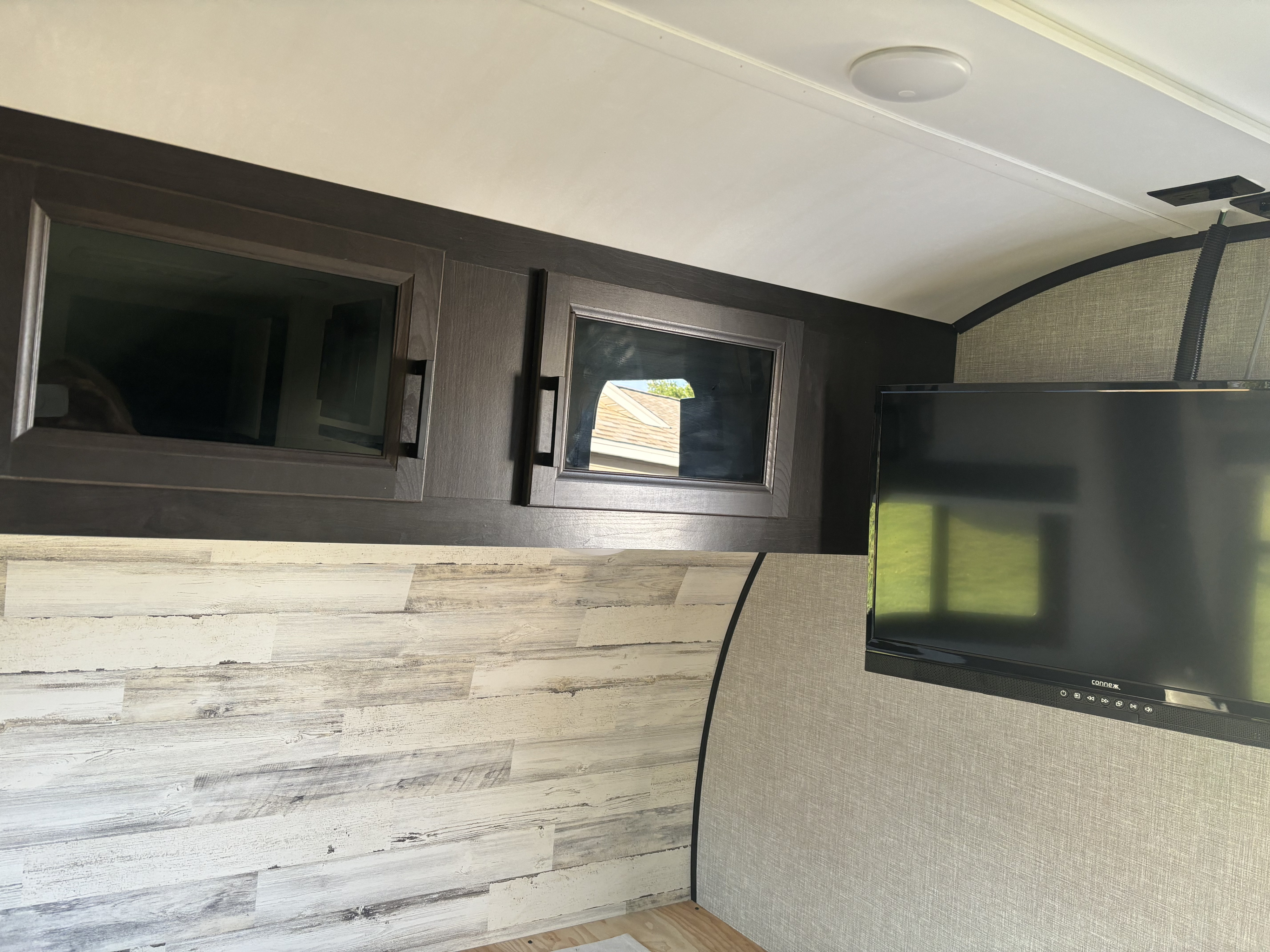 An RV rental interior featuring dark wood overhead cabinets, a mounted TV, and contrasting light wood & textured wall panels.. Jayco Jay Feather Micro 2022