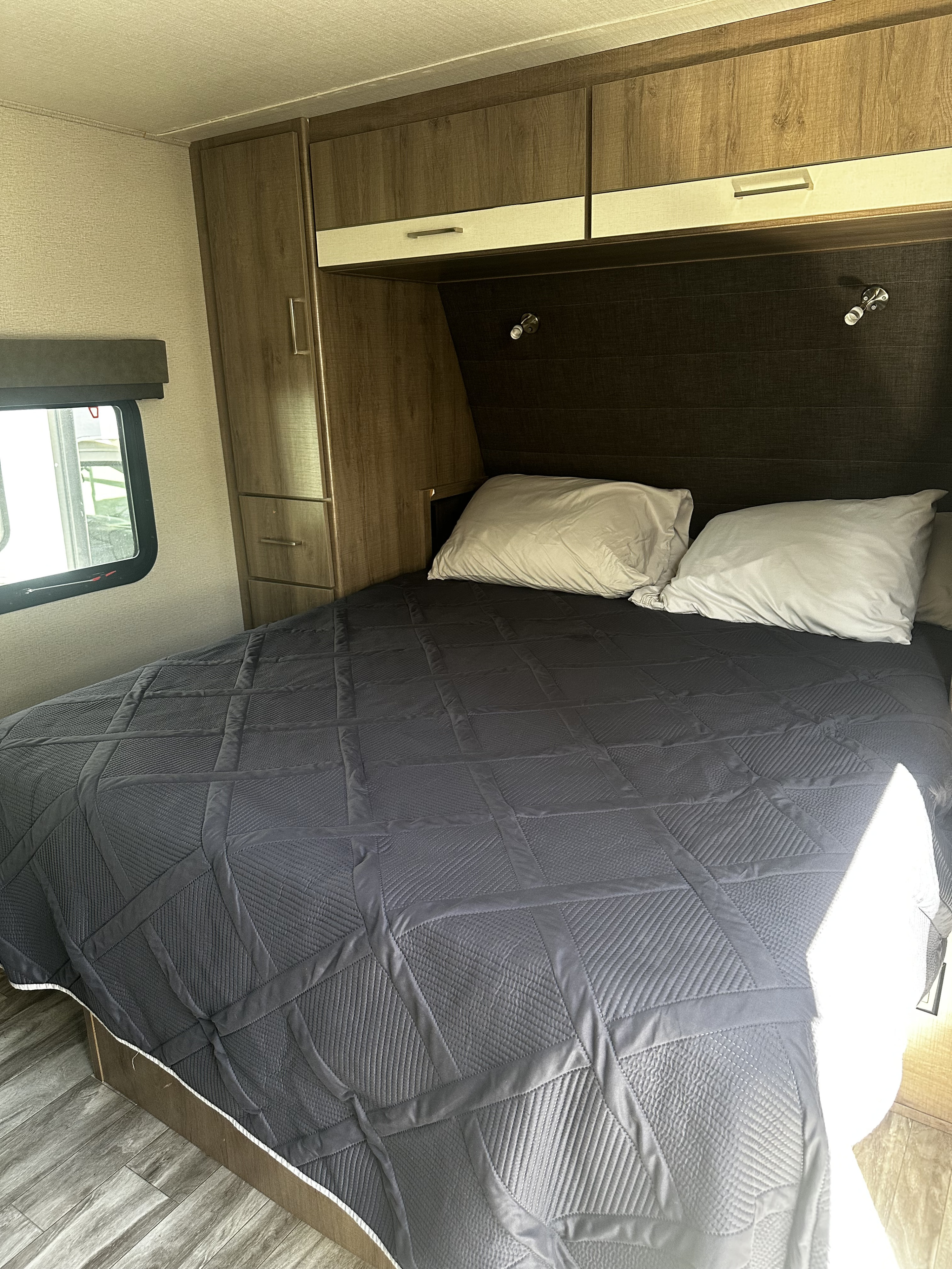Inside a comfortable RV rental bedroom featuring a large bed with a dark gray quilt, pillows, and ample storage cabinets.. Grand Design Imagine XLS 2021