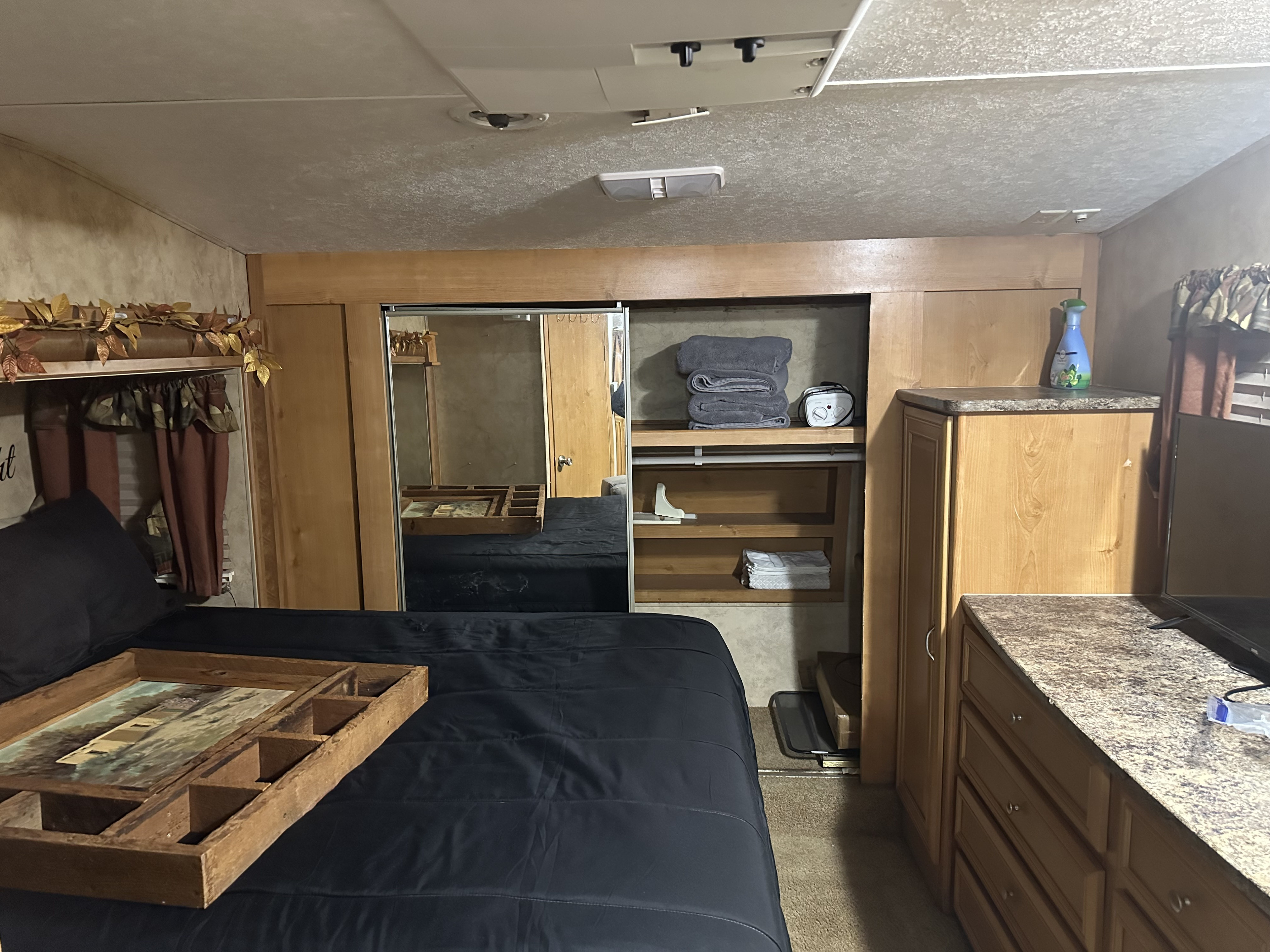 RV rental bedroom with black bed, wooden tray, mirrored closet, open shelves, and light wood cabinetry for storage.. Keystone RV Raptor Toy Hauler 2008