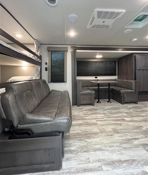 Inside an RV rental, featuring bunk beds, a pull-out sofa, and a dinette with bench seating. Modern interior for travel.. Grand Design Transcend Xplor 265BH 2021