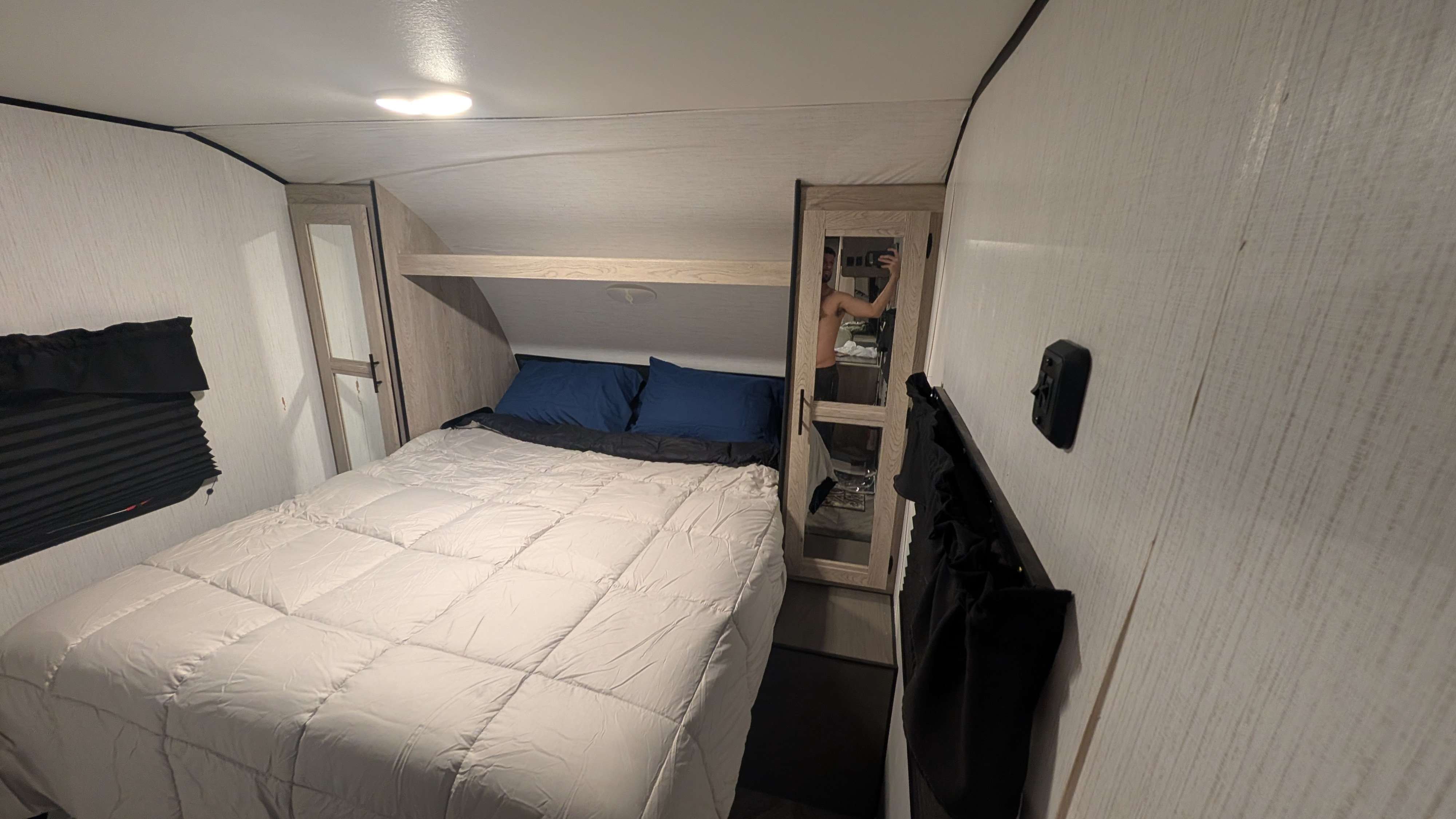 This RV rental bedroom features a comfy bed with a light comforter, blue pillows, and a mirrored closet, offering a modern interior.. Heartland RVs Prowler 2022