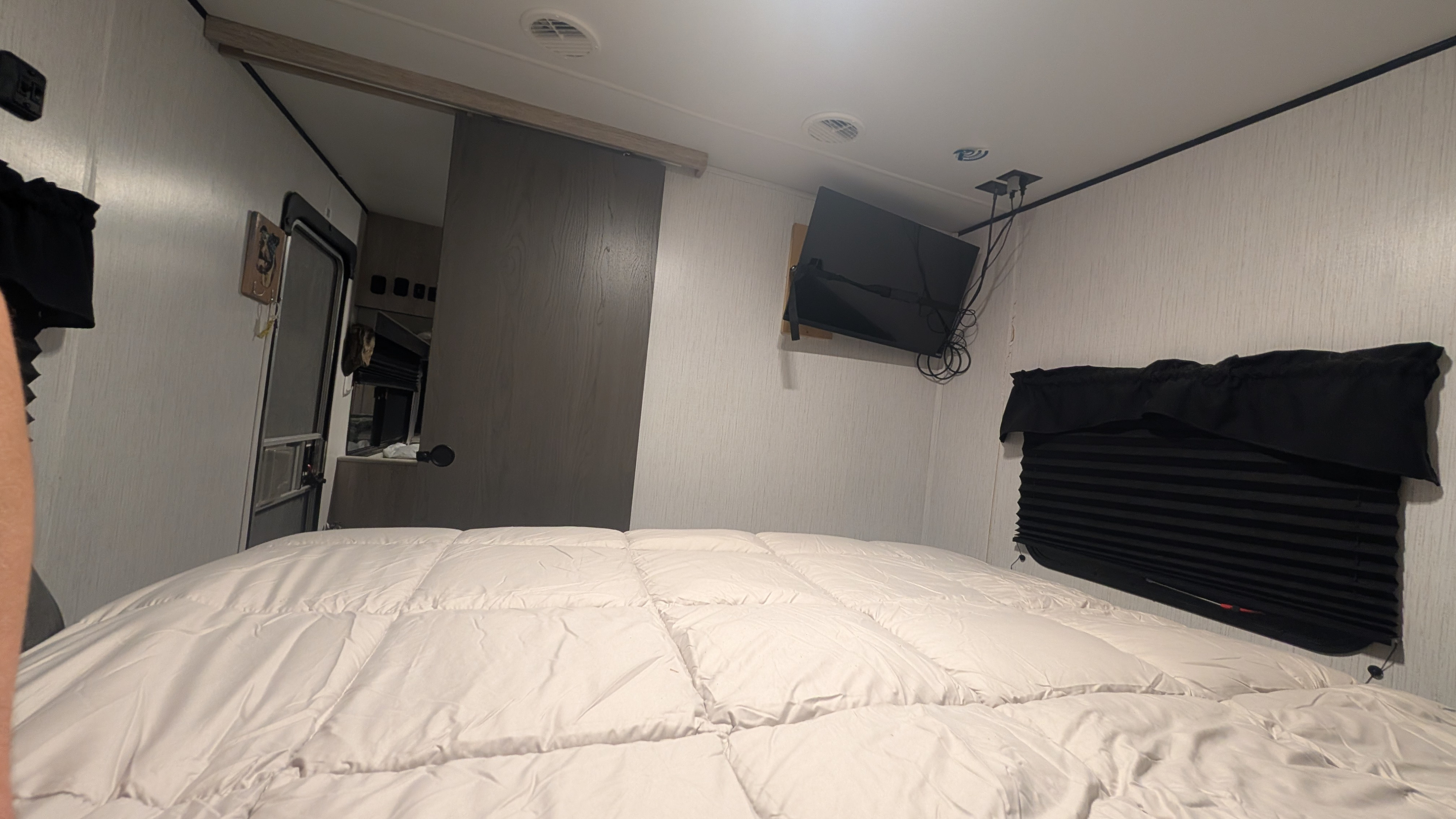 RV rental bedroom features a comfy bed, mounted TV, and black-out blinds, showcasing compact RV living.. Heartland RVs Prowler 2022