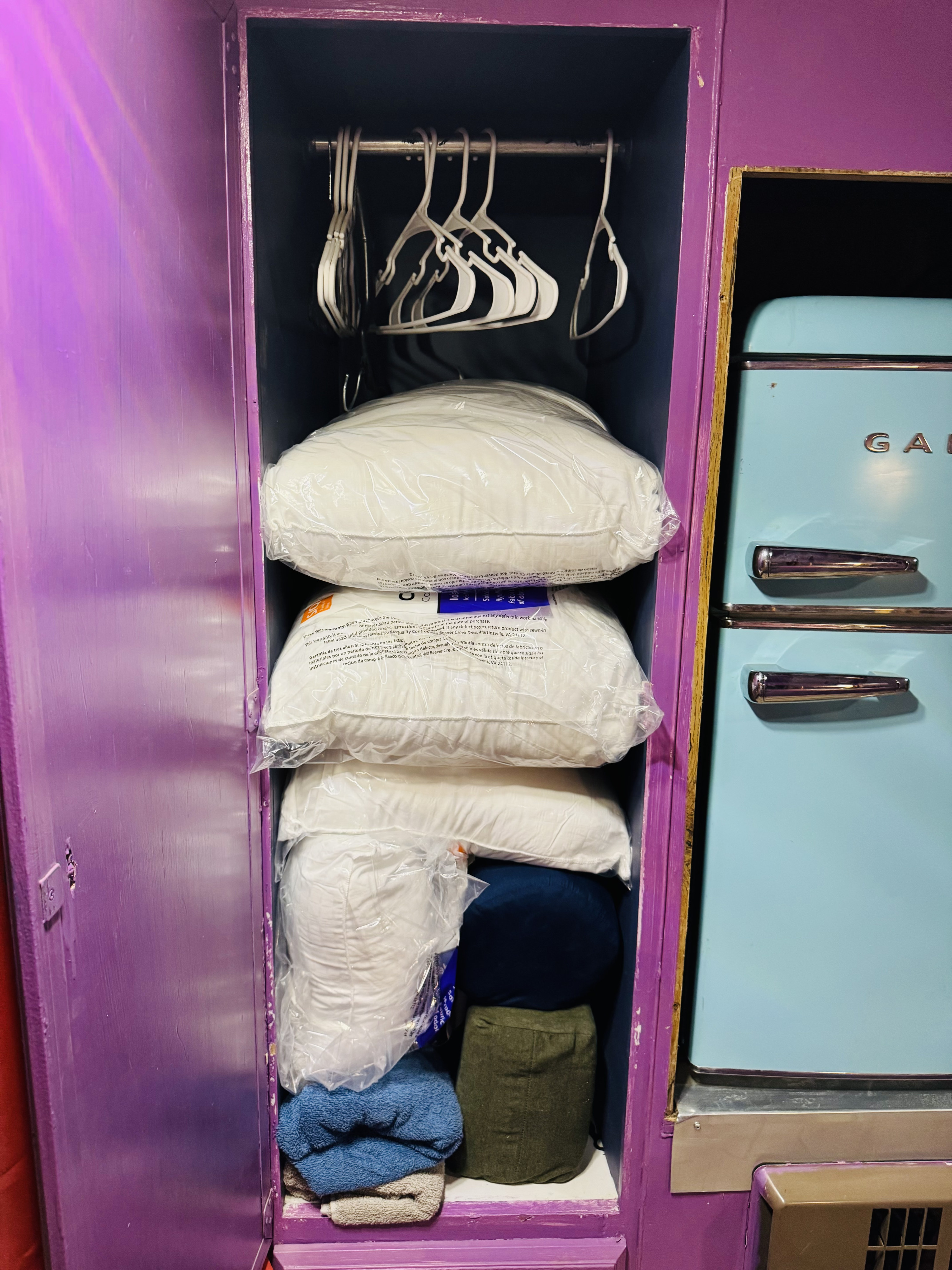 RV rental storage: A purple cabinet holds hangers, new pillows, and towels next to a light blue mini-fridge.. Kit Kit Trailer Deluxe 1978