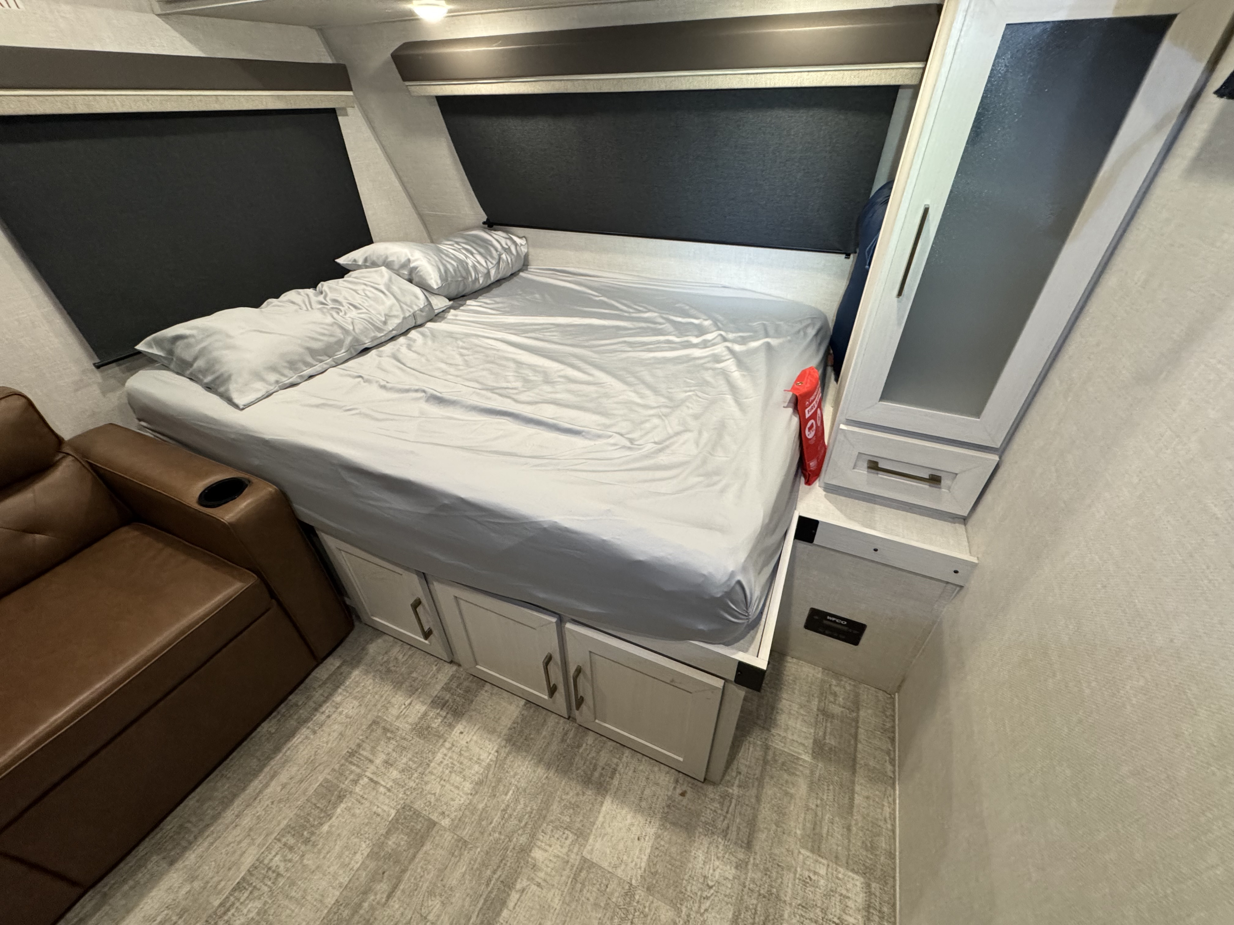 Spacious RV rental bedroom with a light gray bed, under-bed storage, brown reclining sofa, and blackout blinds.. Forest River No Boundaries 18.0 with beastmode 2025