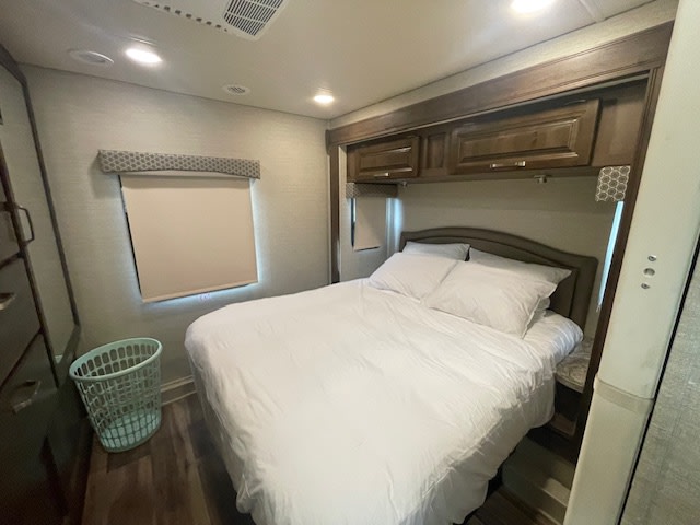 This RV rental features a cozy bedroom with a comfortable bed, overhead cabinets, and a window for natural light.. Jayco Greyhawk 2019