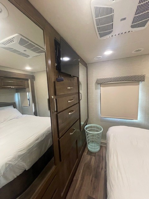 RV rental interior view of a bedroom with two beds, a mounted TV, and wooden storage cabinets.. Jayco Greyhawk 2019