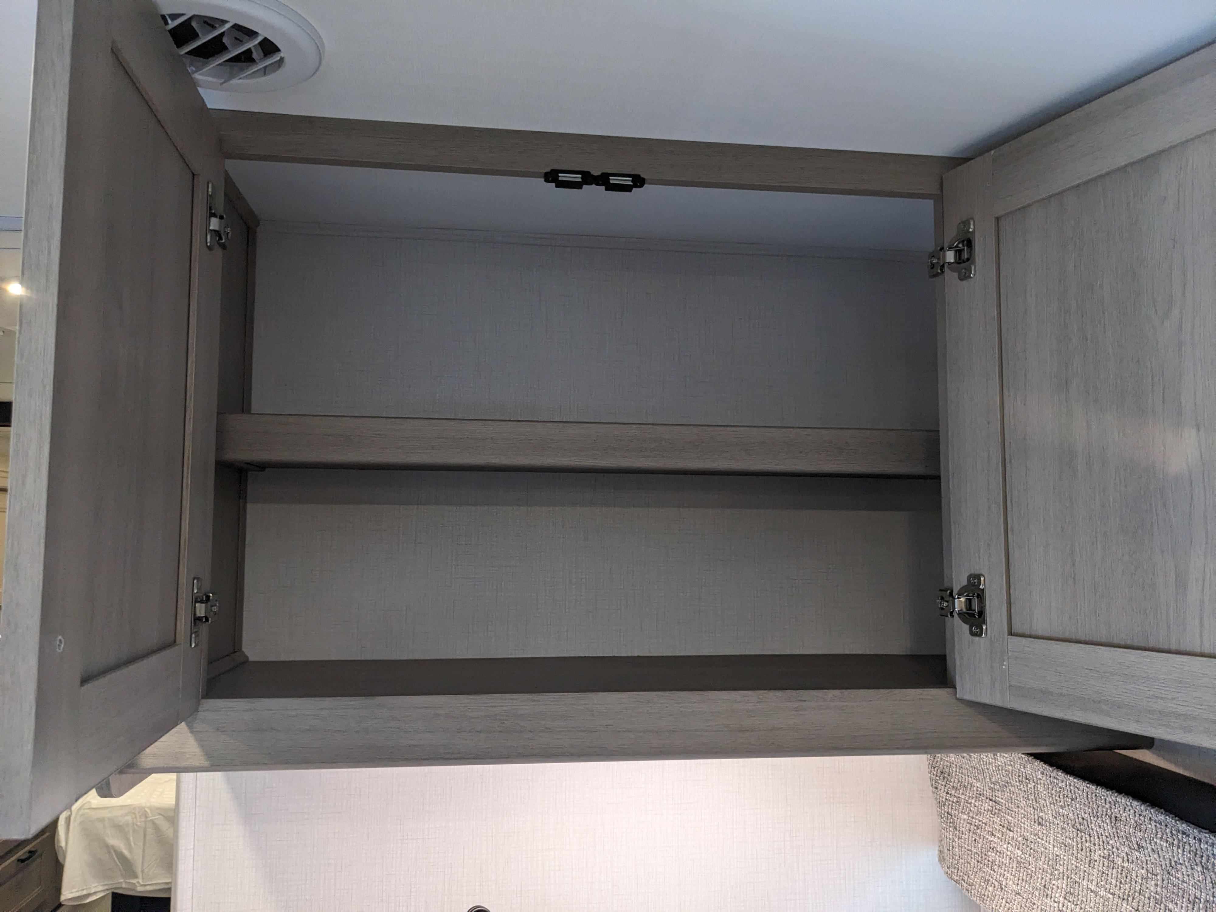 Open RV rental overhead cabinet with two shelves, magnetic latches, and a vent, offering essential storage for travel.. Forest River Forester 2027