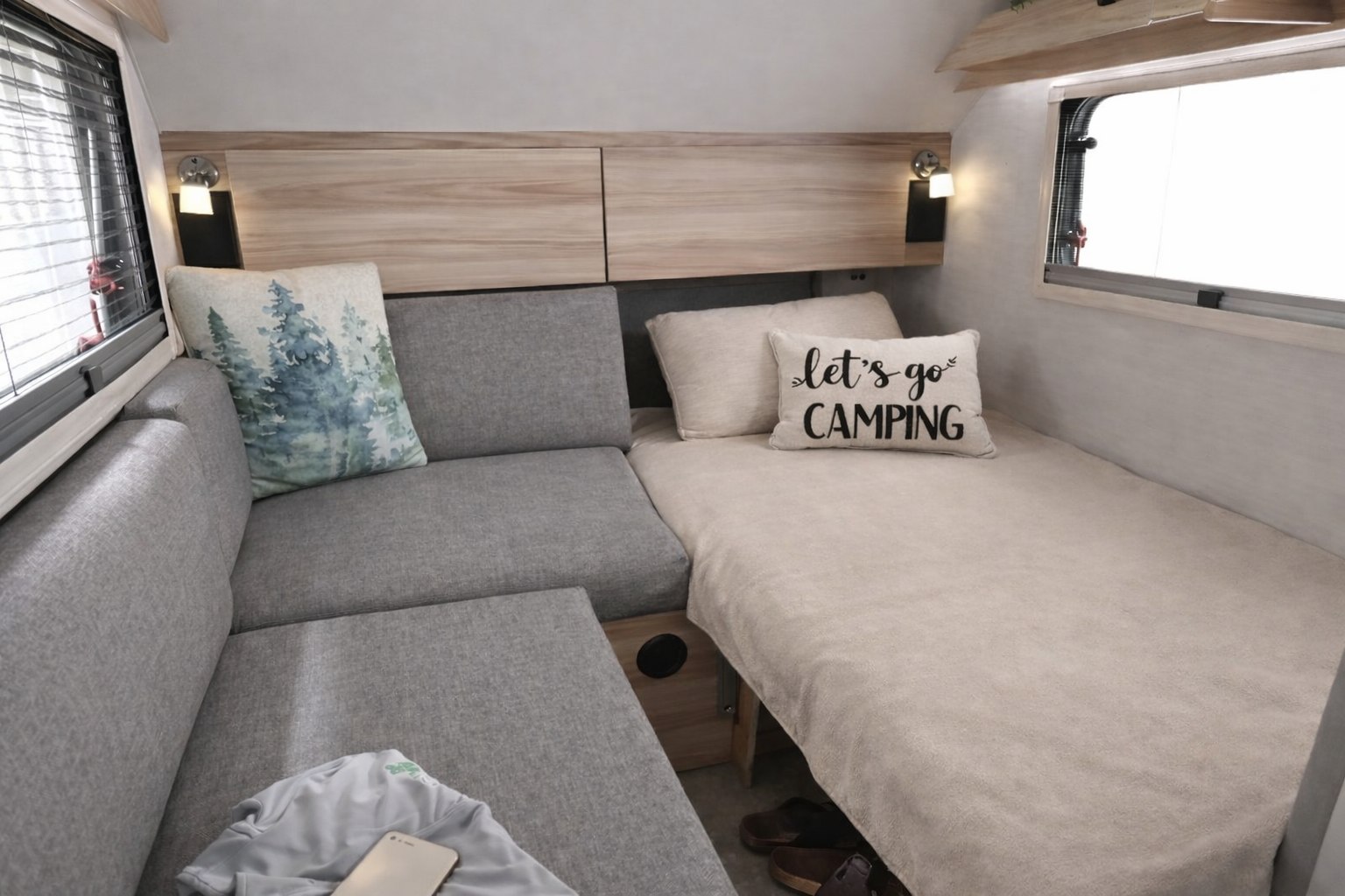 Cozy RV rental interior: L-shaped sofa, bed with "let's go CAMPING" pillow, and wooden cabinets for comfortable travel.. nuCamp T@B 2024