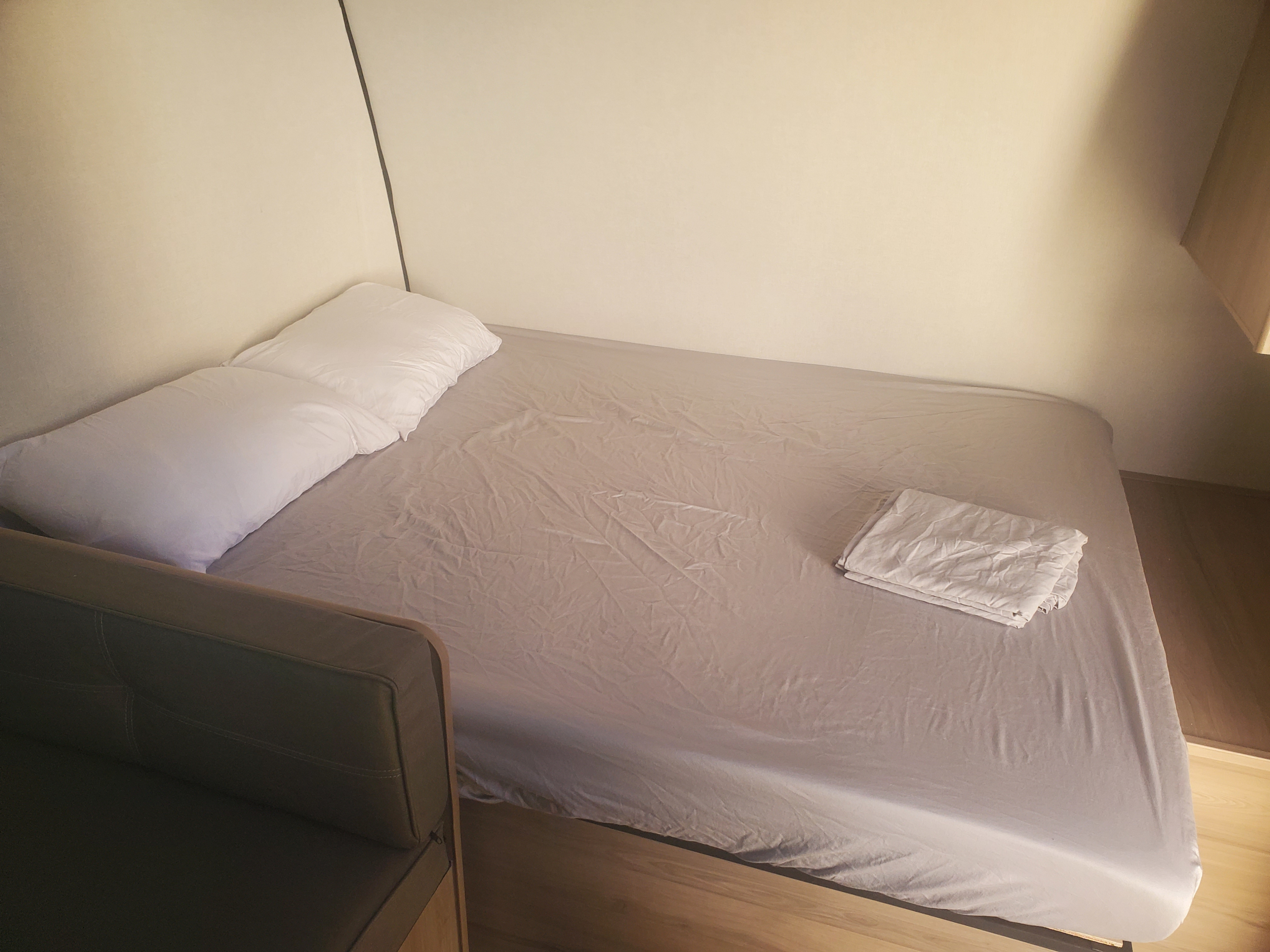 Compact sleeping area in an RV rental: a bed with two white pillows, gray sheets, folded linens, and a dark couch.. Keystone RV Coleman 2026