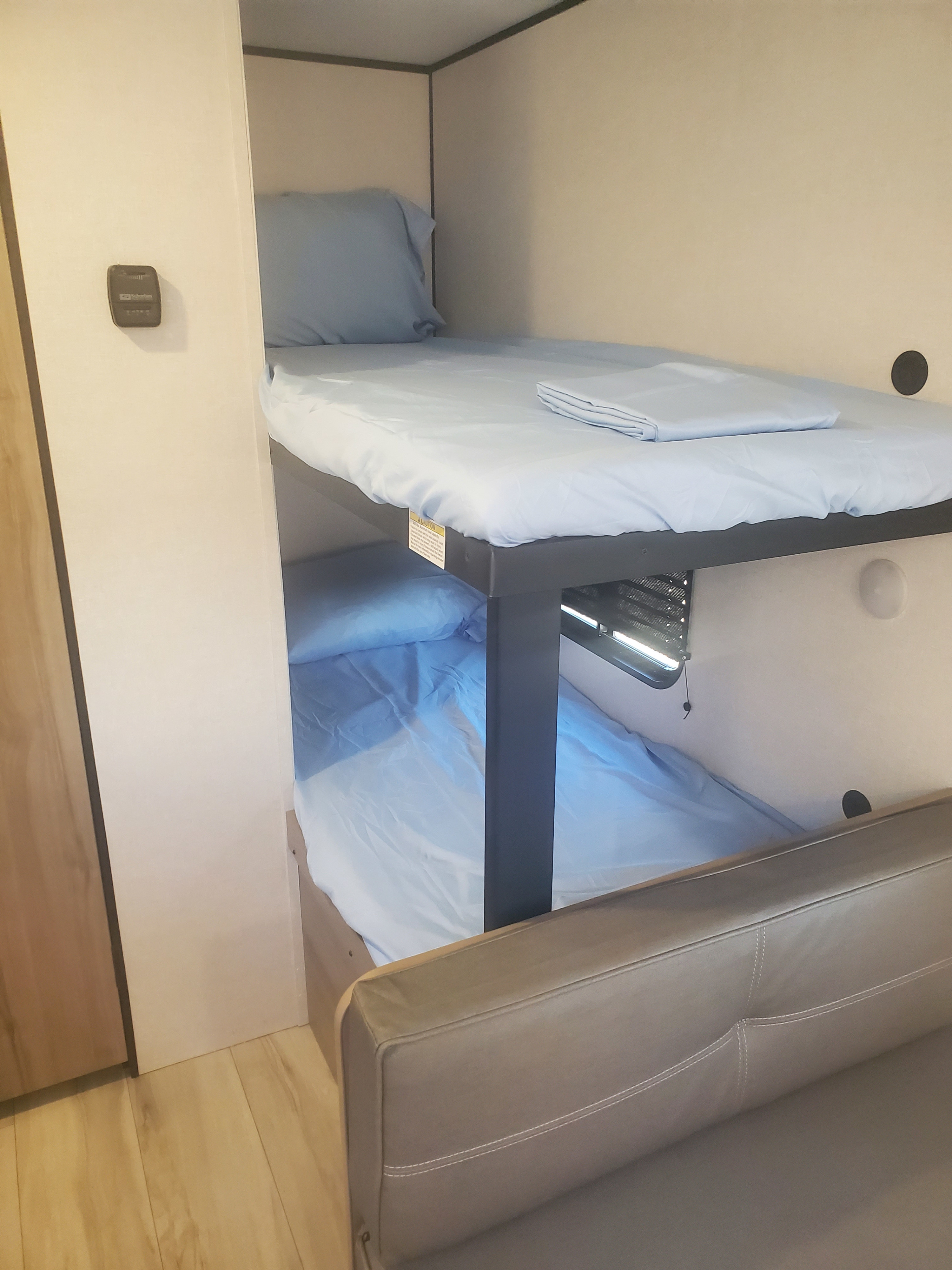 Cozy RV rental interior featuring bunk beds with fresh blue linens, a climate control panel, and a soft couch.. Keystone RV Coleman 2026