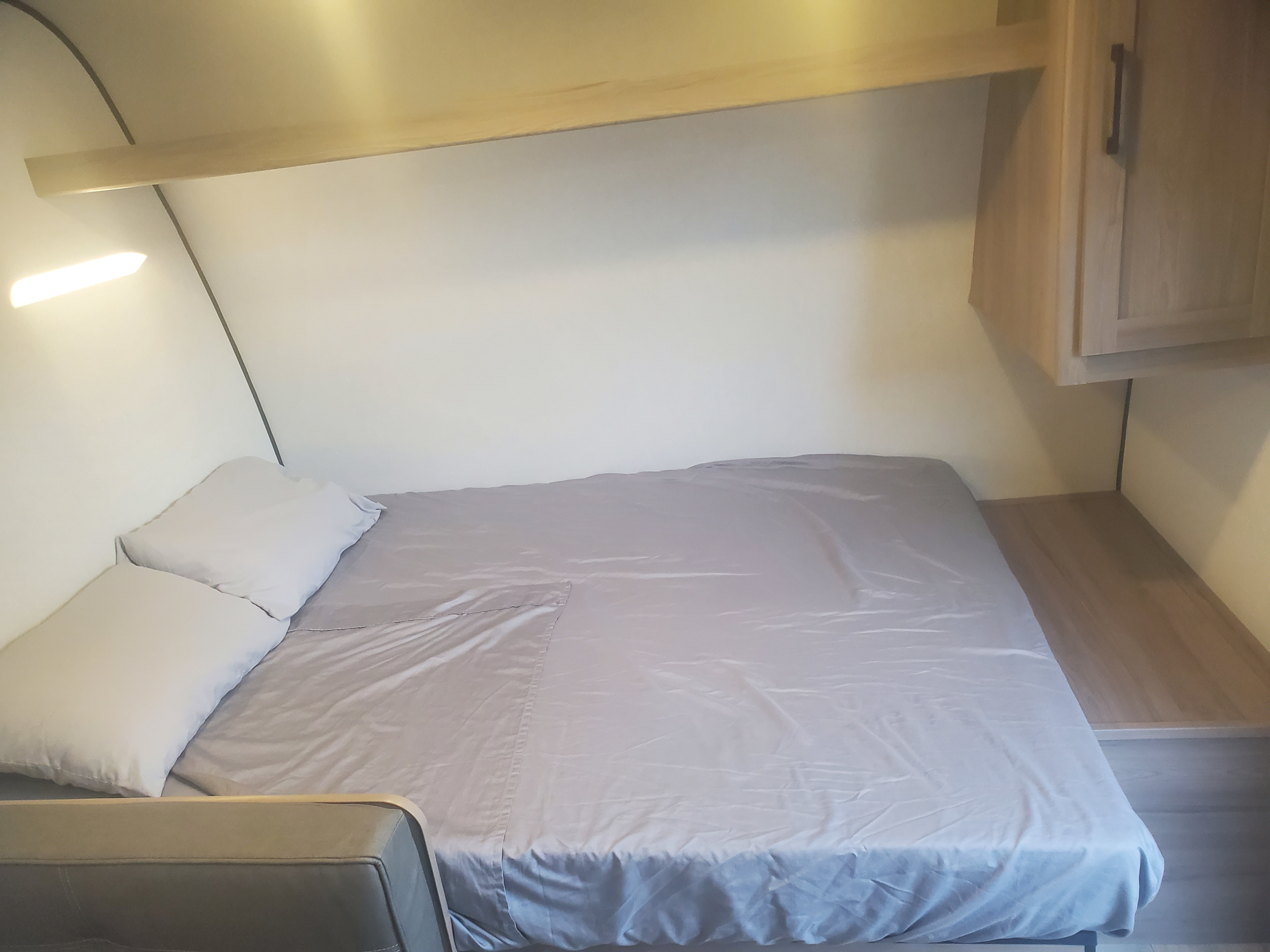 Cozy sleeping area in an RV rental, featuring a bed with light gray sheets, pillows, an overhead shelf, and cabinet.. Keystone Coleman 2026