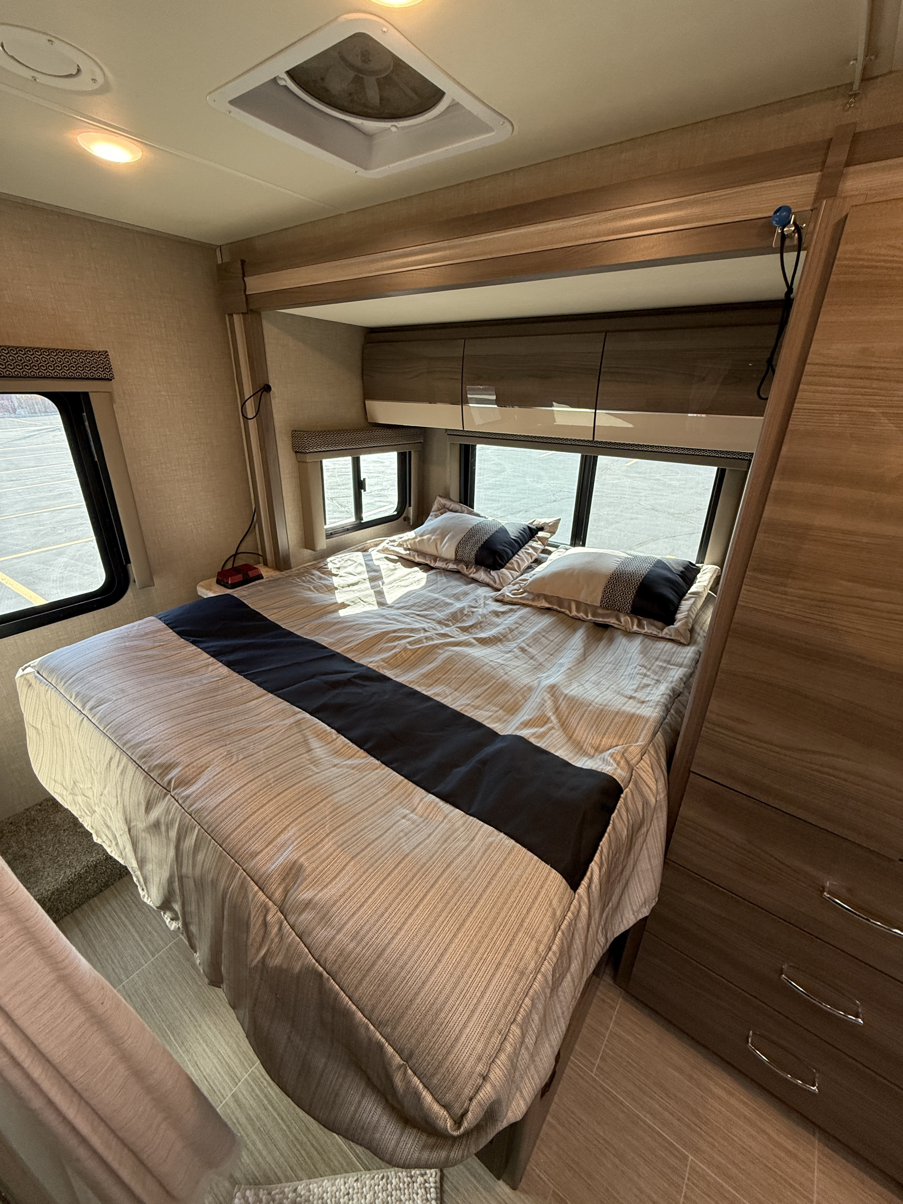 Experience comfort in this modern RV rental bedroom featuring a queen bed, storage, and natural light from windows.. Thor Delano 2021