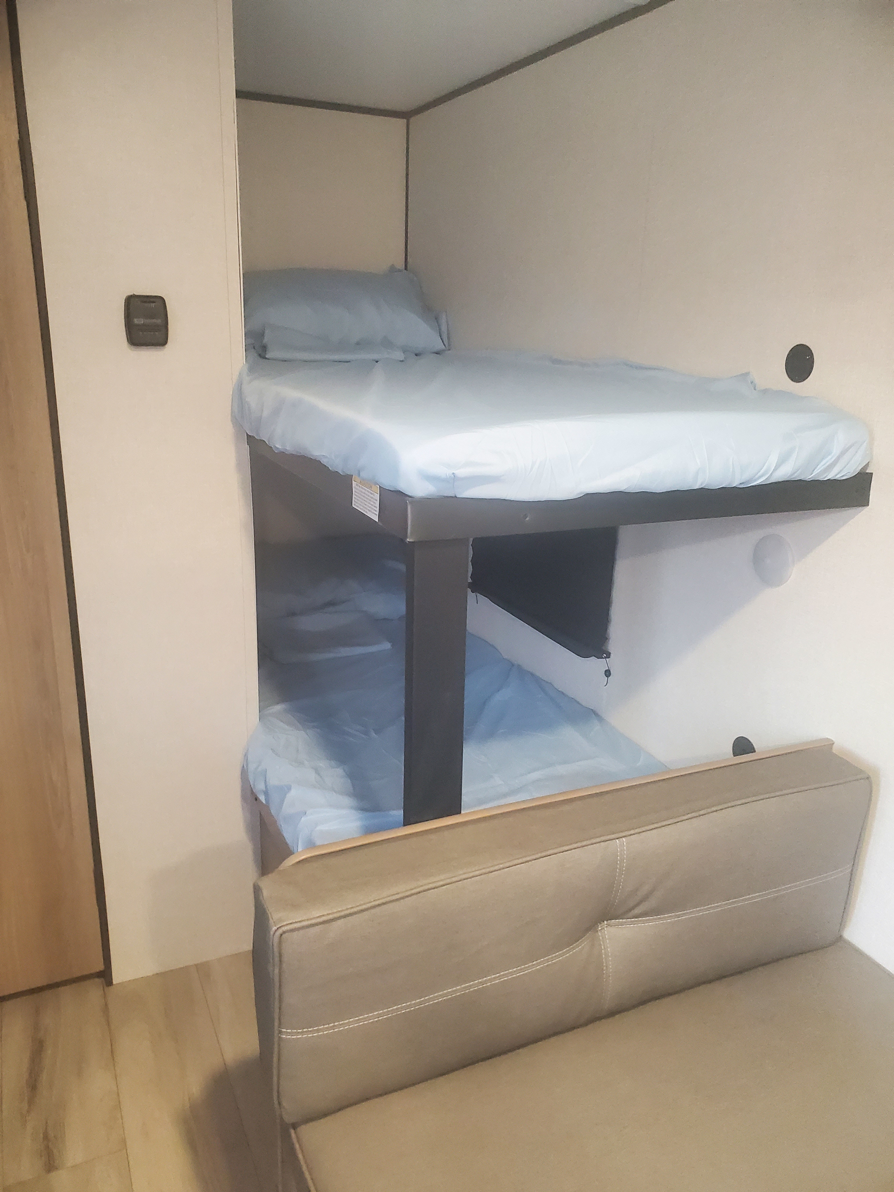 RV rental with functional bunk beds (light blue bedding), a thermostat, and a beige sofa. Ideal compact sleeping area.. Keystone Coleman 2026