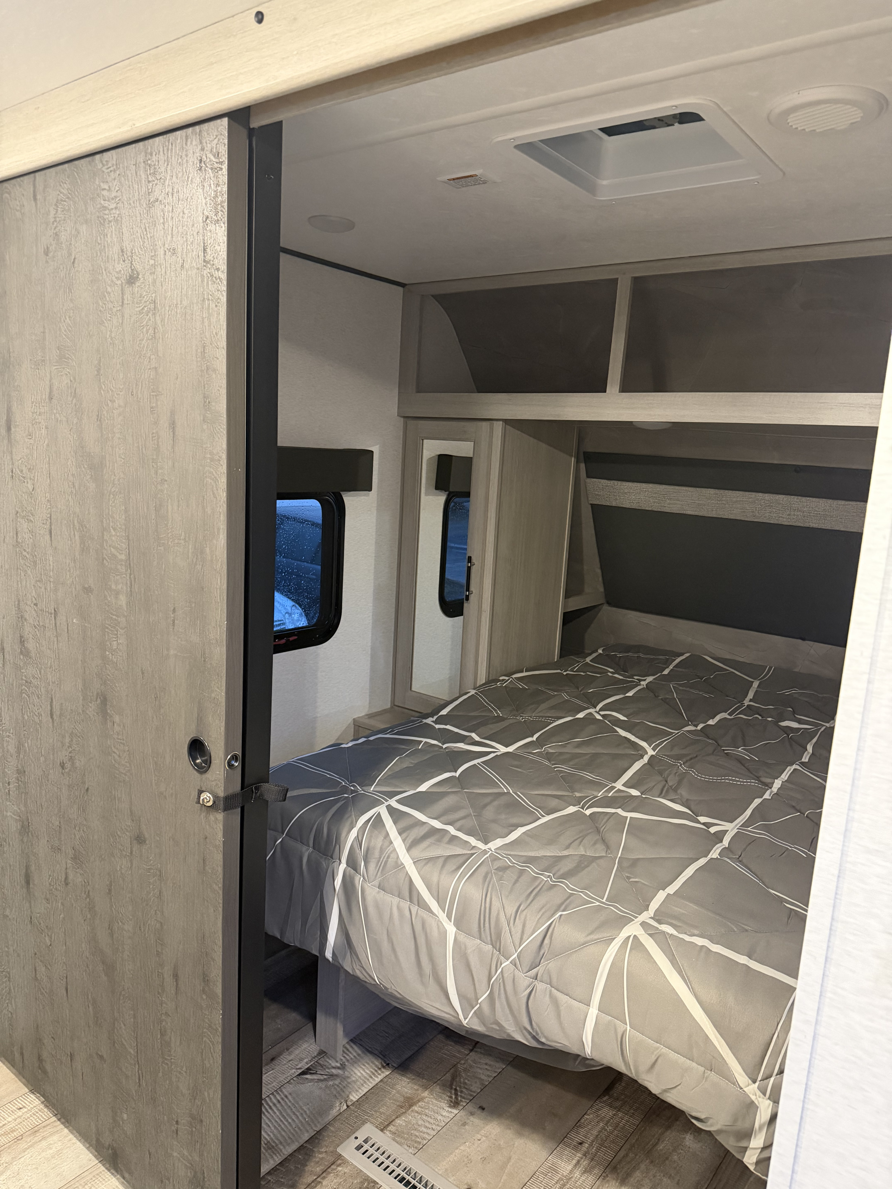 Inside an RV rental: view of a compact bedroom with a bed, sliding door, and overhead storage.. Crossroads RV Sunset Trail Sport 2025