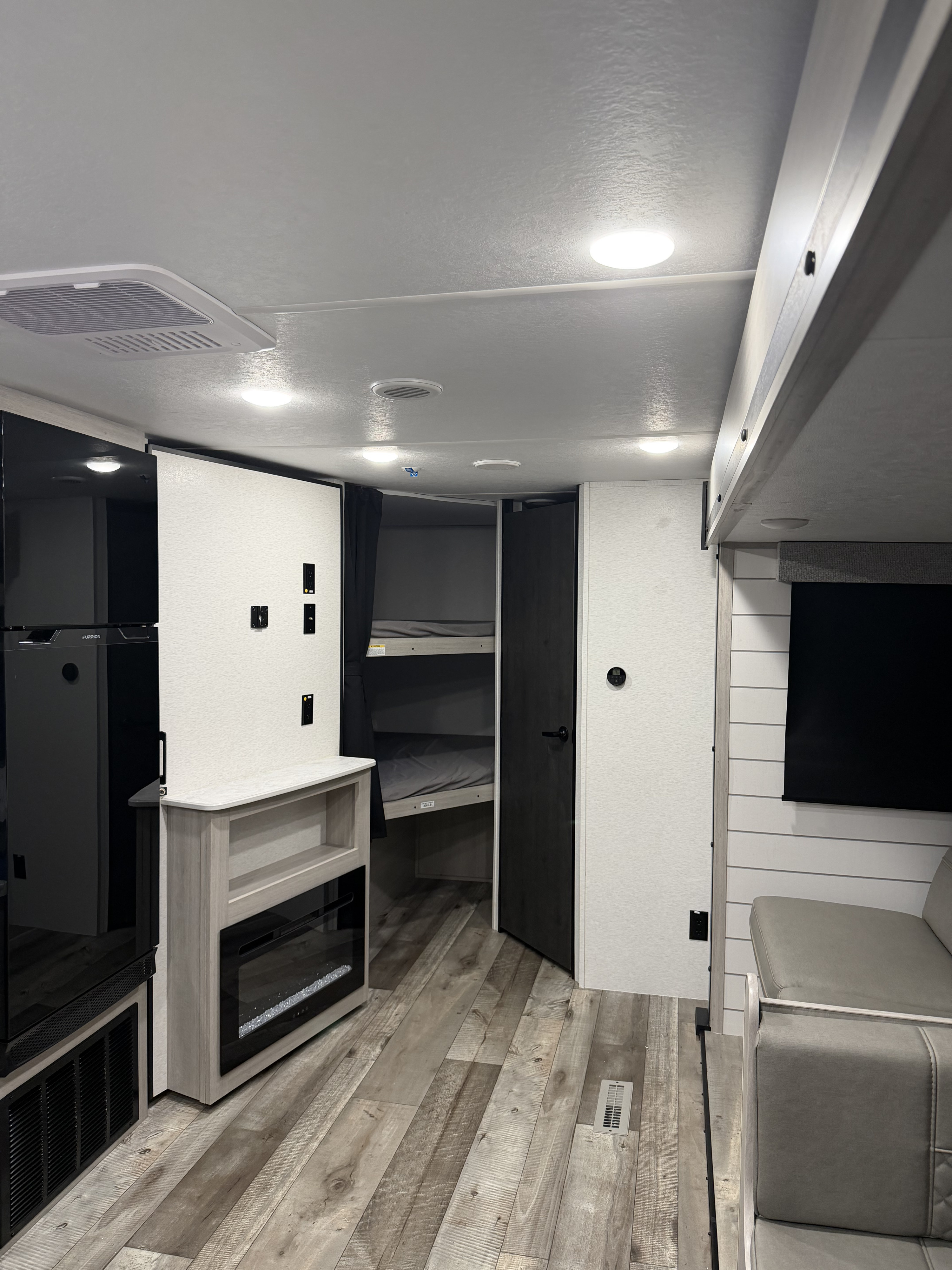 Modern RV rental interior with bunk beds, refrigerator, fireplace, and sofa. Bright, spacious living area.. Crossroads RV Sunset Trail Sport 2025