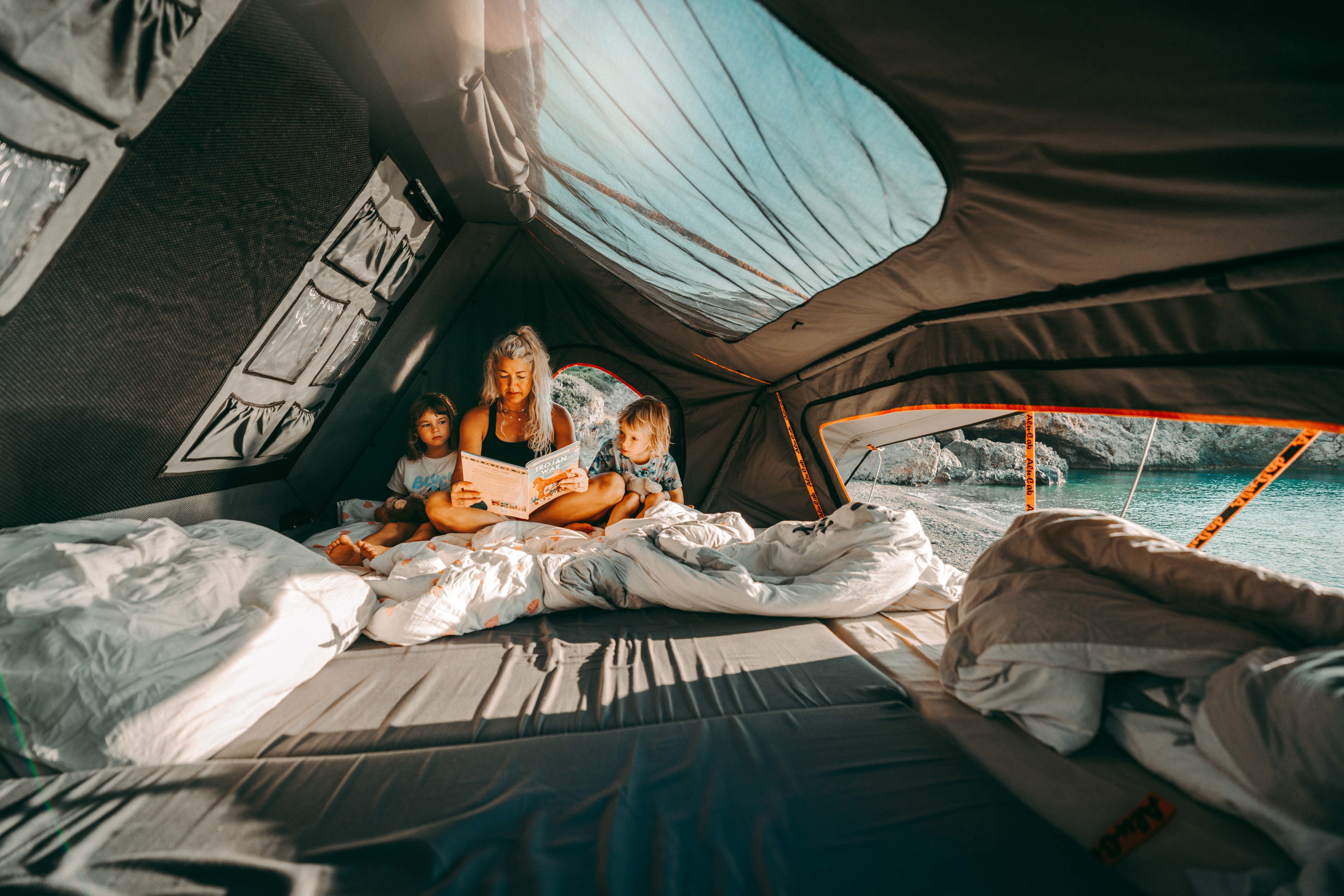 Family time in an RV rental rooftop tent. Mom reads "Trojan War" to kids, enjoying a beautiful sea view from their cozy bed.. Toyota Tundra 2019