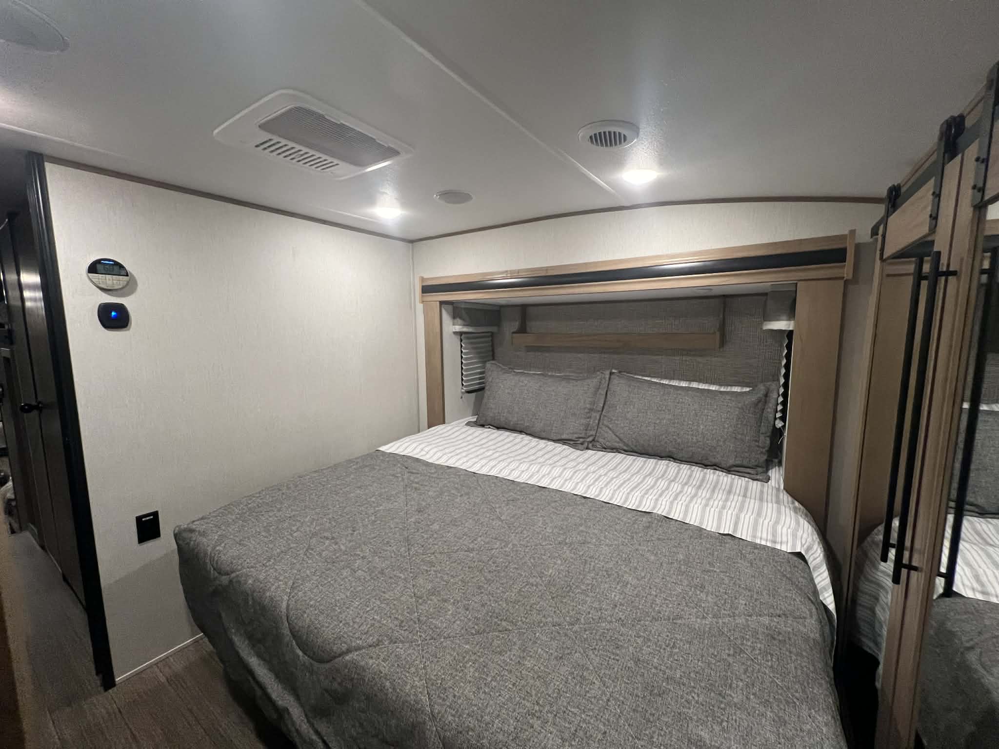 Modern RV rental bedroom featuring a comfy bed with grey bedding, overhead lighting, AC, and built-in storage.. Forest River Sabre 2023