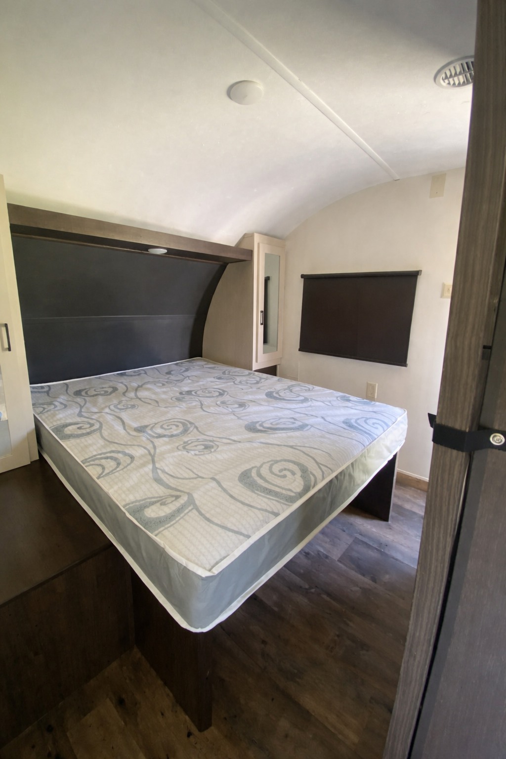 Cozy RV rental bedroom: patterned mattress on a platform, built-in storage, wood flooring, and curved ceiling.. Forest River Wildwood 2018