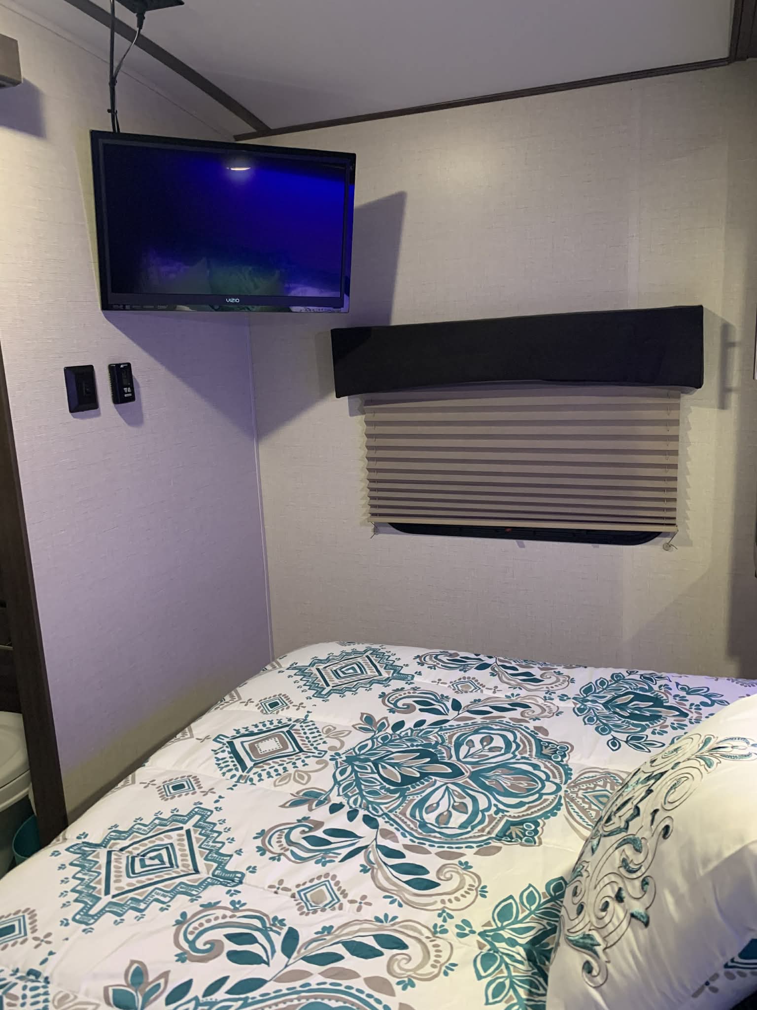 RV rental bedroom: Mounted TV, cozy bed with a teal and grey patterned comforter, and window blind for comfortable travel.. Crossroads RV Sunset Trail Super Lite 2018