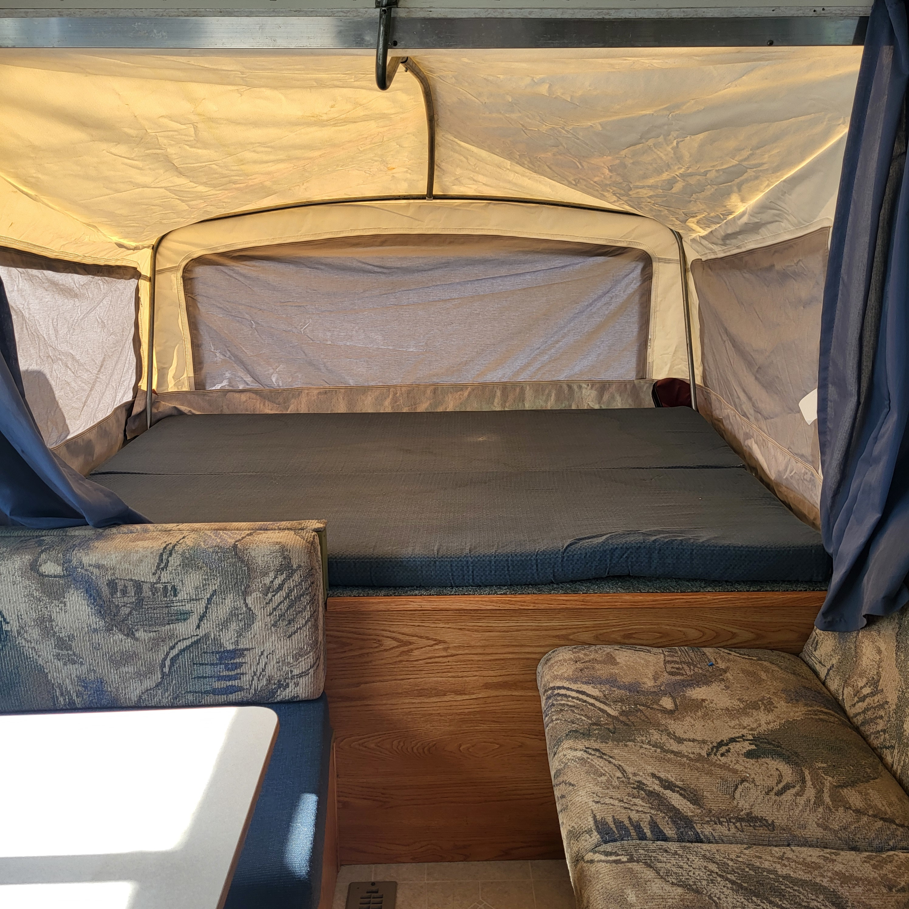 Pop-up RV rental interior: a comfy bed, dinette seating, and canvas walls filled with warm light for your trip.. Dutchmen Sport 2002