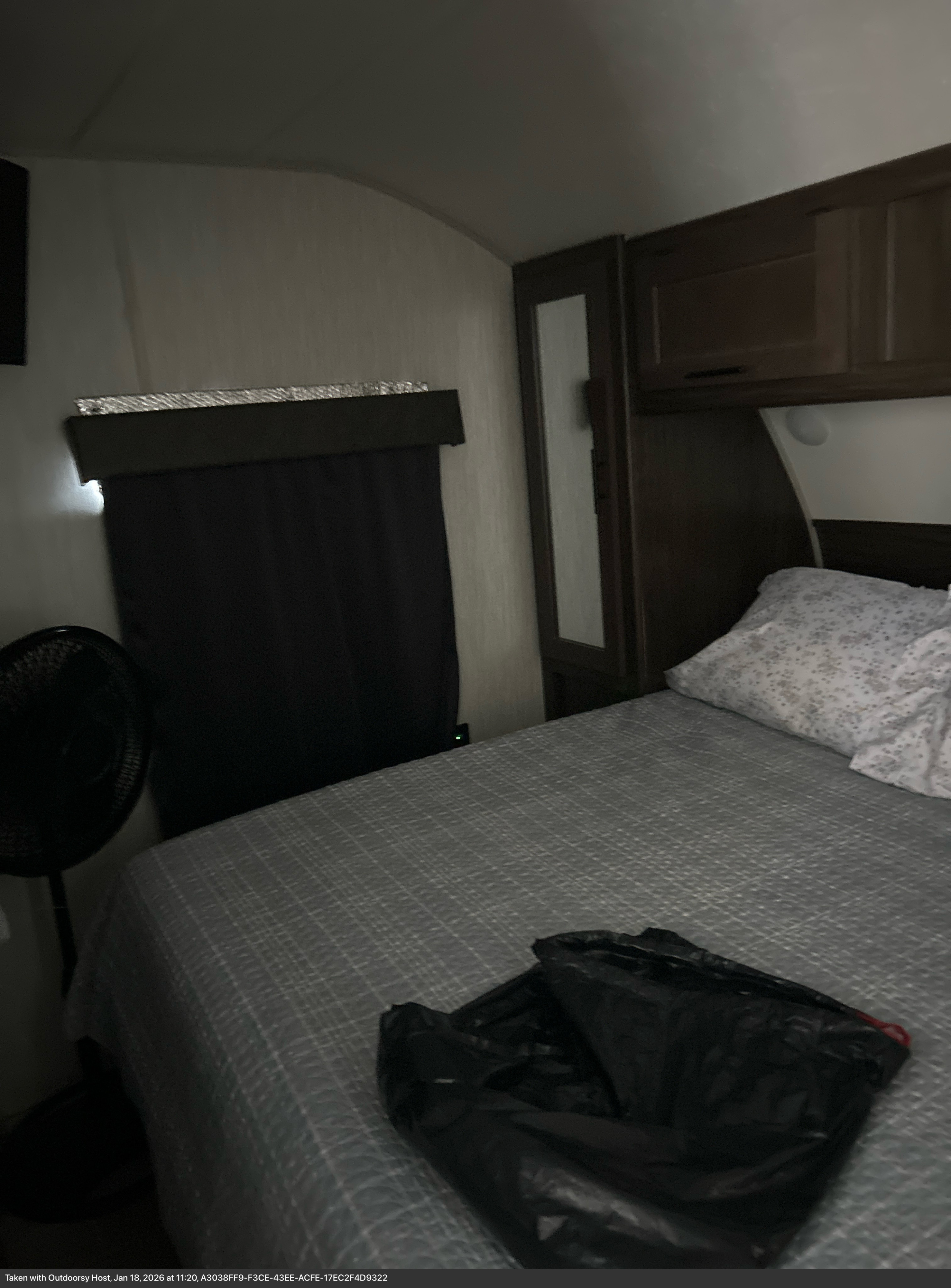 Cozy RV rental bedroom with a bed, dark curtains, overhead cabinets, and a fan on the left, offering a comfortable stay.. Forest River Cherokee Grey Wolf 2021