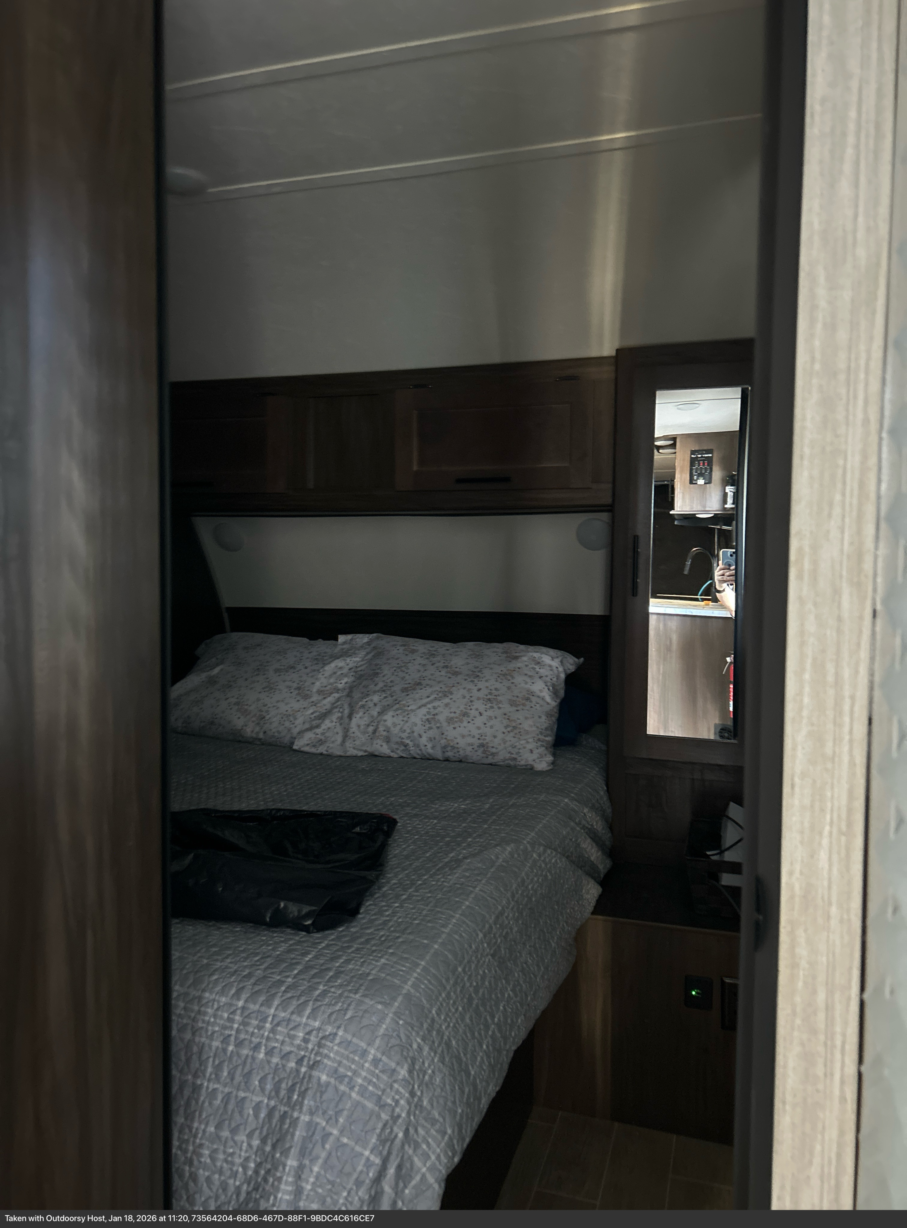 Cozy RV rental bedroom featuring a queen bed, overhead cabinets, and a mirror reflecting the kitchen area.. Forest River Cherokee Grey Wolf 2021