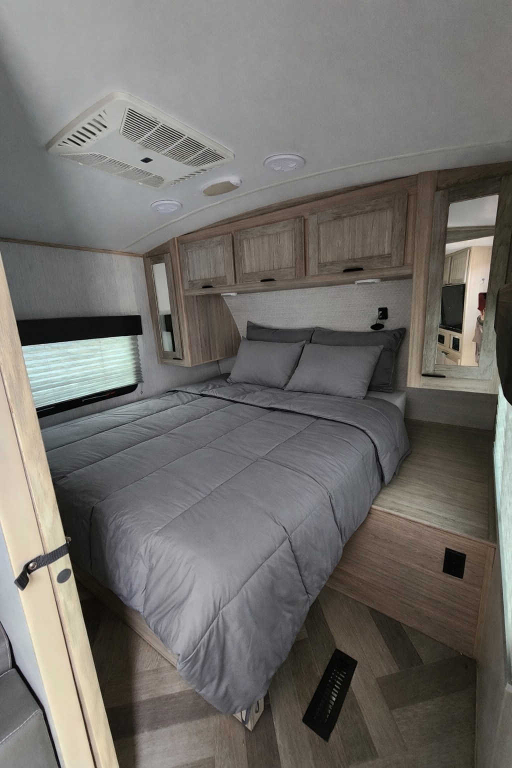 Comfortable gray queen bed in an RV rental bedroom with overhead wood cabinets & AC. Ideal travel accommodations.. Heartland RVs Cruiser 2022