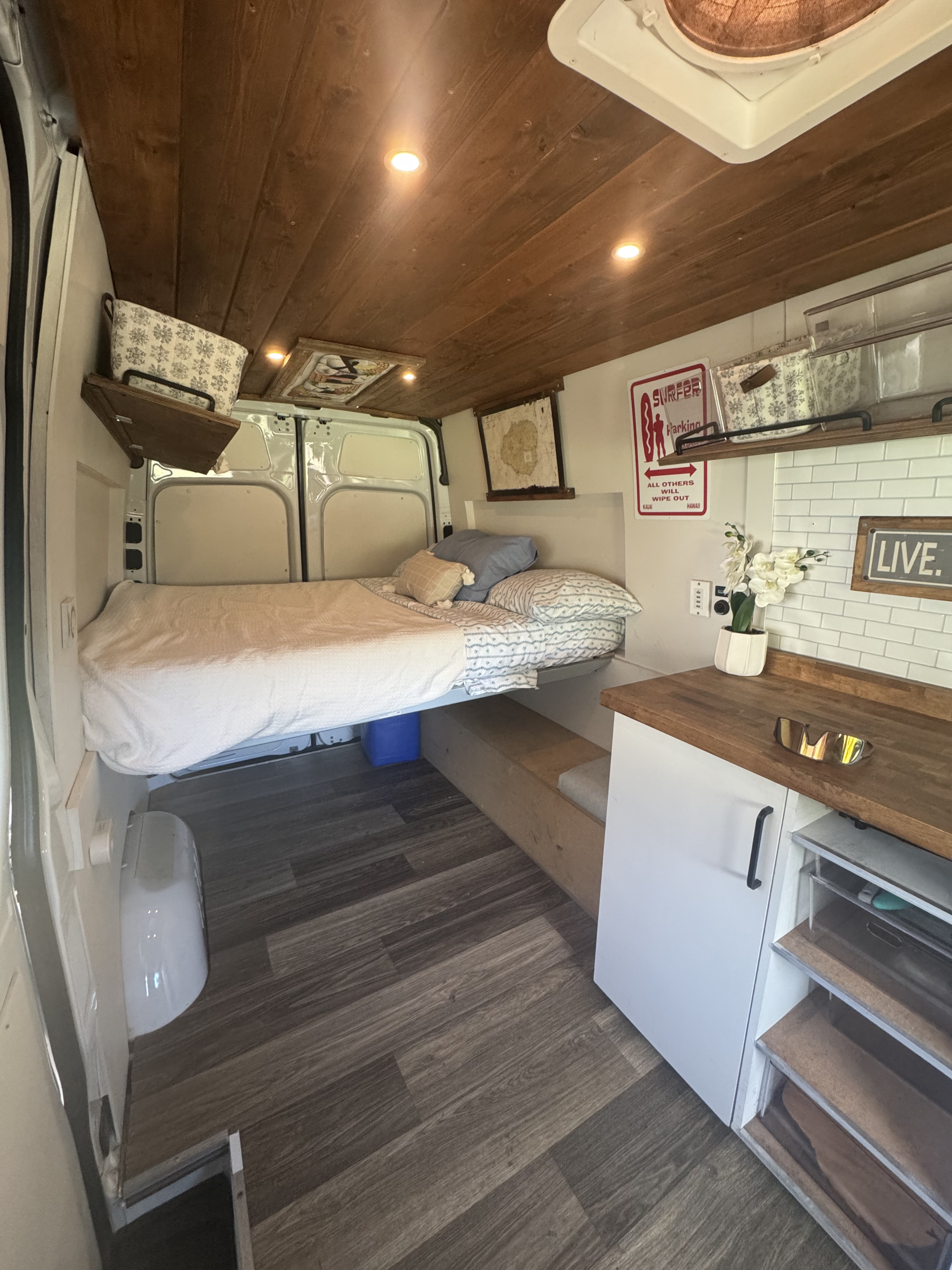 Custom rv rental campervan interior with cozy bed, wood plank ceiling, functional counter, & stylish dark wood floor.. Mercedes-Benz Sprinter 2020