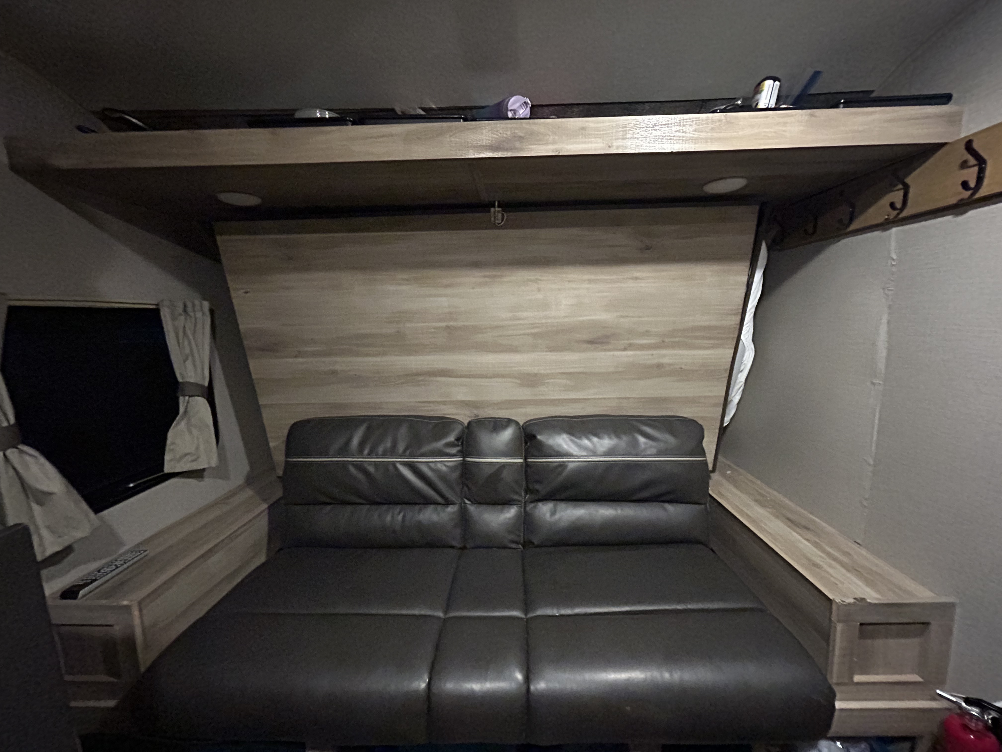 Inside an RV rental: dark leatherette couch converts to a bed, with an overhead bunk and window. Practical RV living space.. Coachmen Catalina Summit 2021