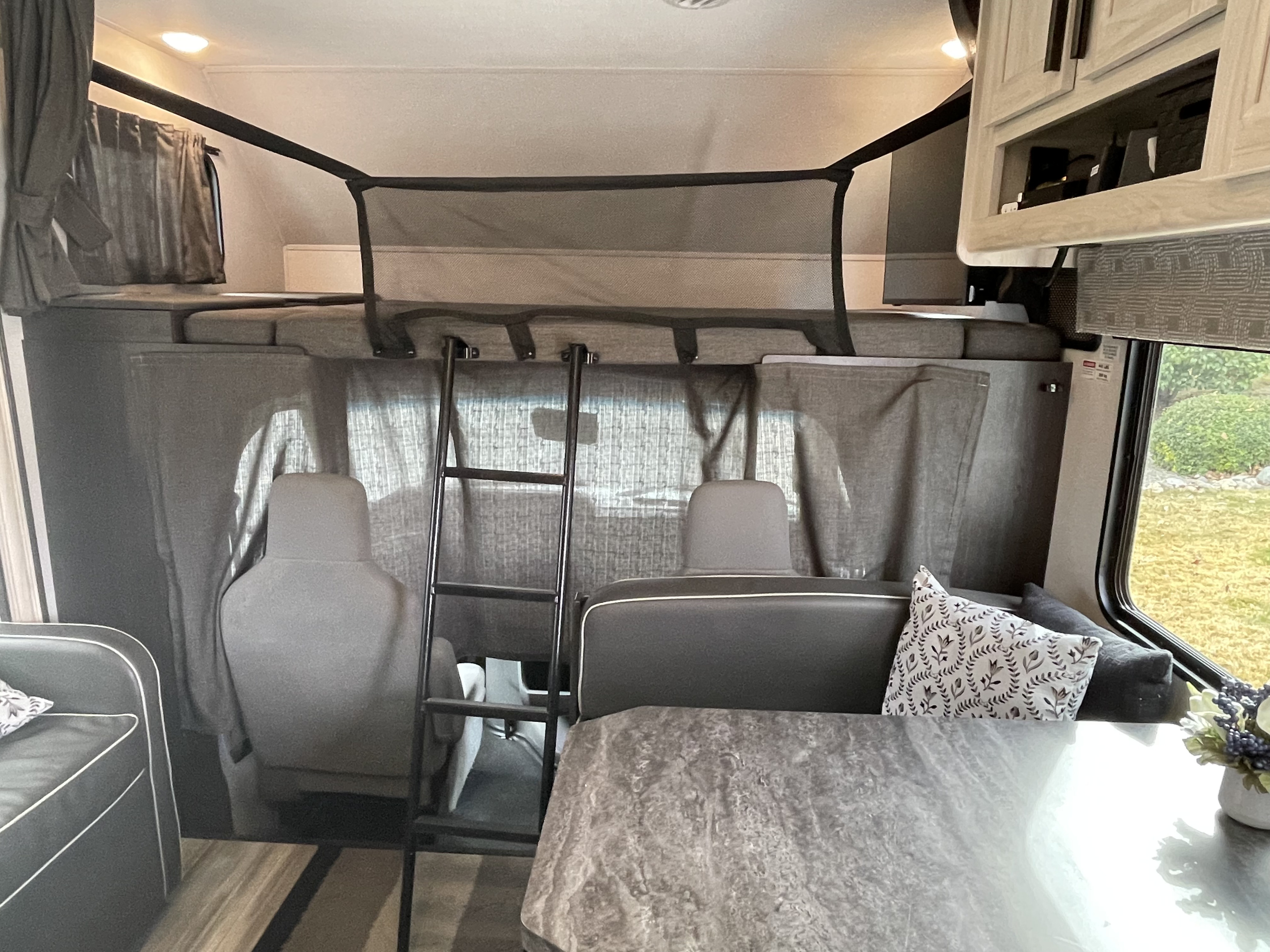 Explore this cozy RV rental interior featuring an over-cab bunk bed with safety net, ladder, and comfortable dining area.. Forest River Sunseeker LE 2024
