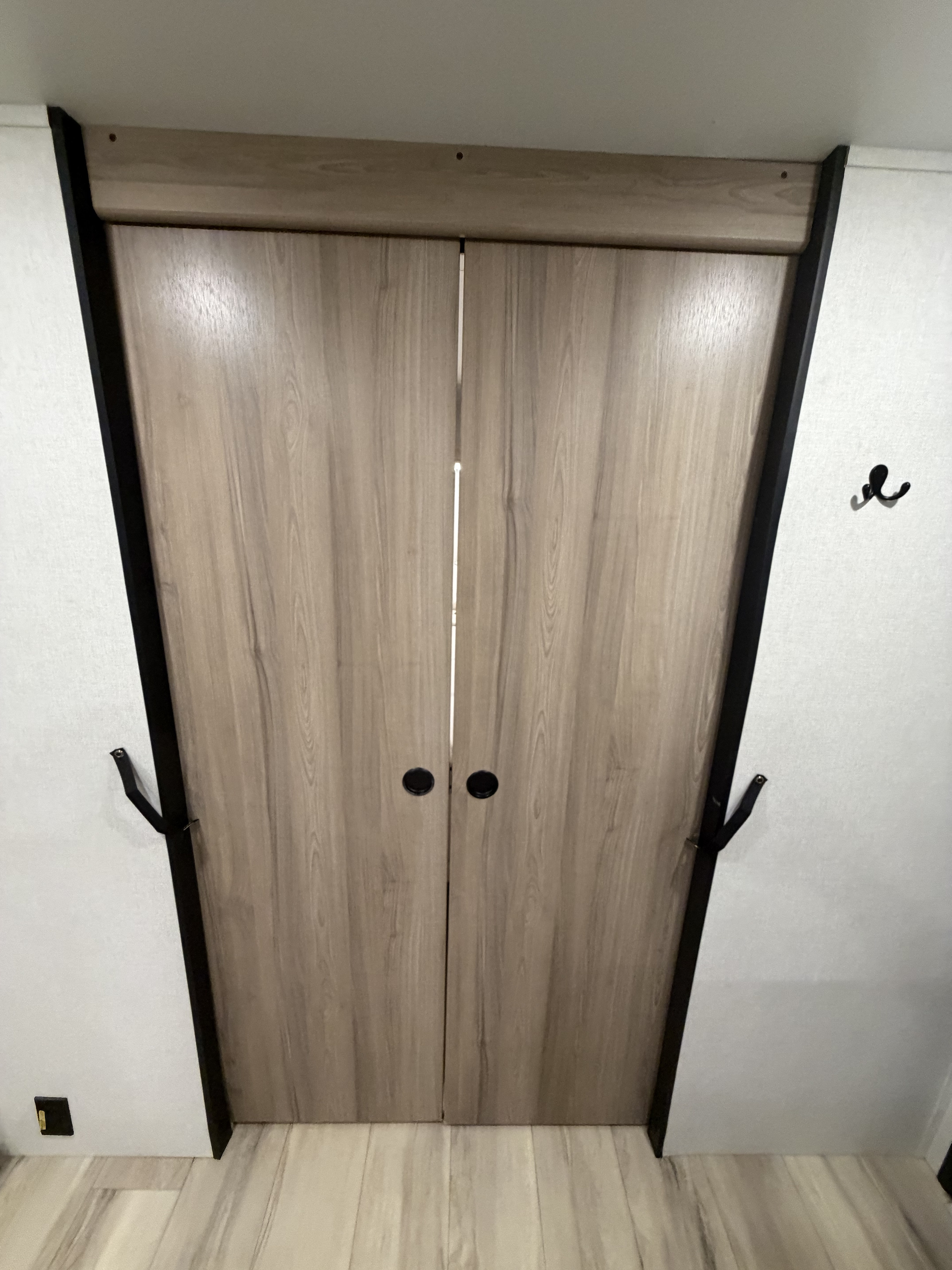 RV rental closet doors: Light wood-grain double doors with black knobs, dark trim, and side securing straps for travel.. Keystone RV Coleman 2025