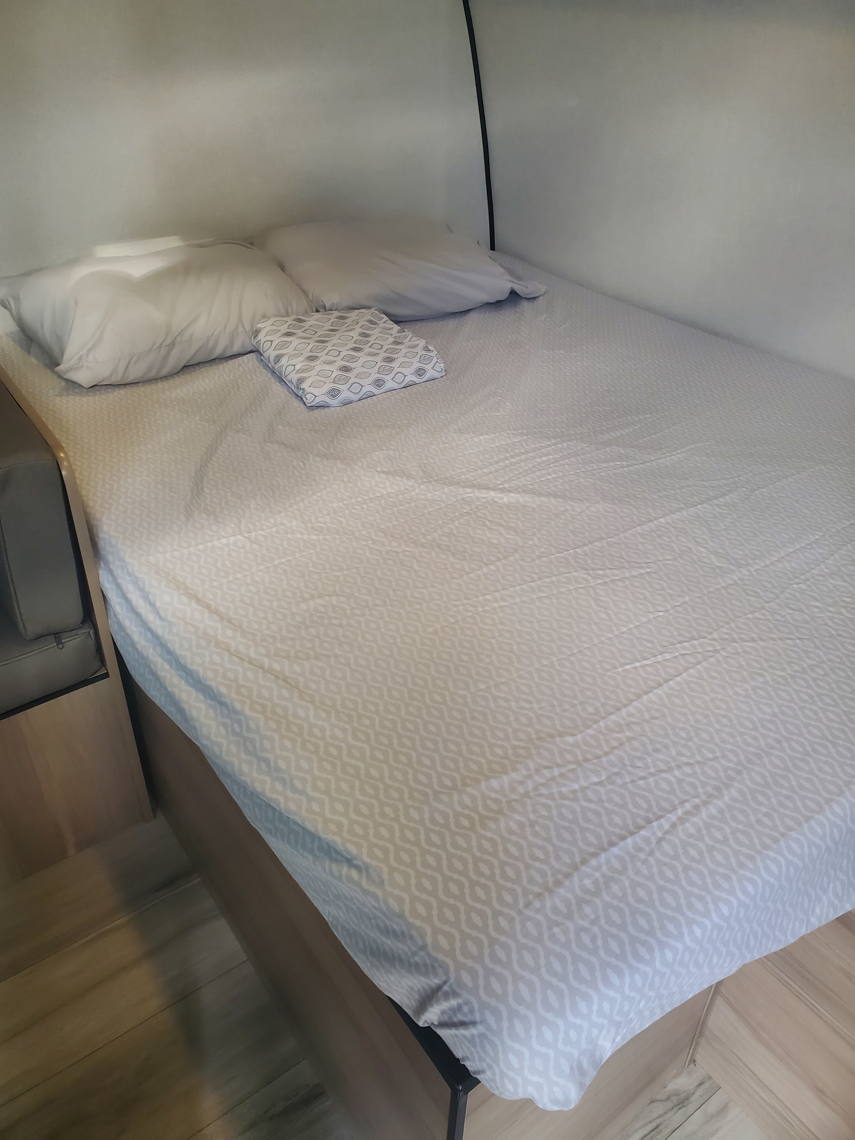 Cozy RV rental bed with light patterned sheets and pillows, offering a comfortable sleeping area inside for travelers.. Keystone Coleman 2026