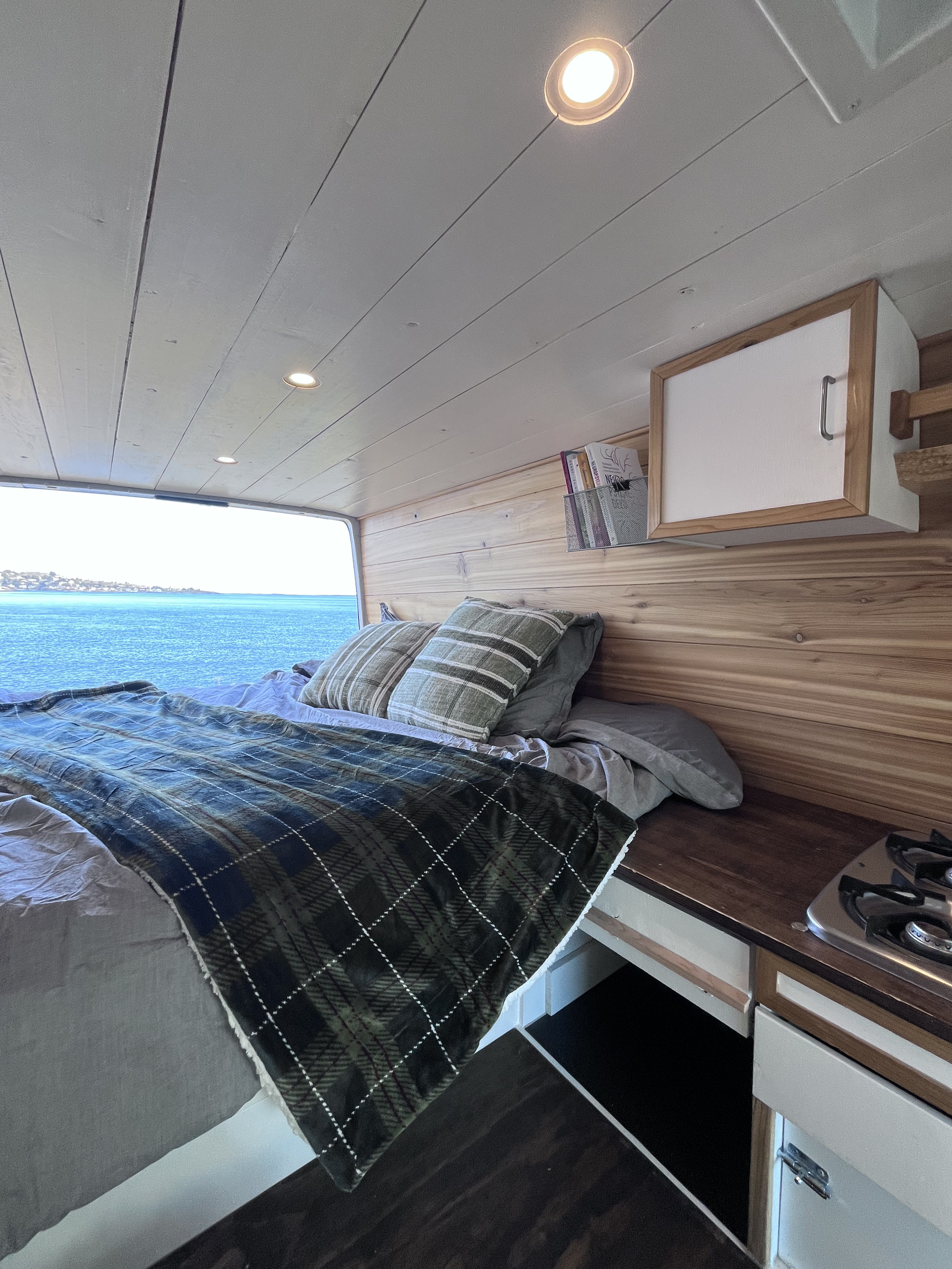 Enjoy this RV rental's cozy interior: a bed with ocean view, compact kitchen, wooden walls, & recessed lighting.. Dodge Sprinter Van 2005
