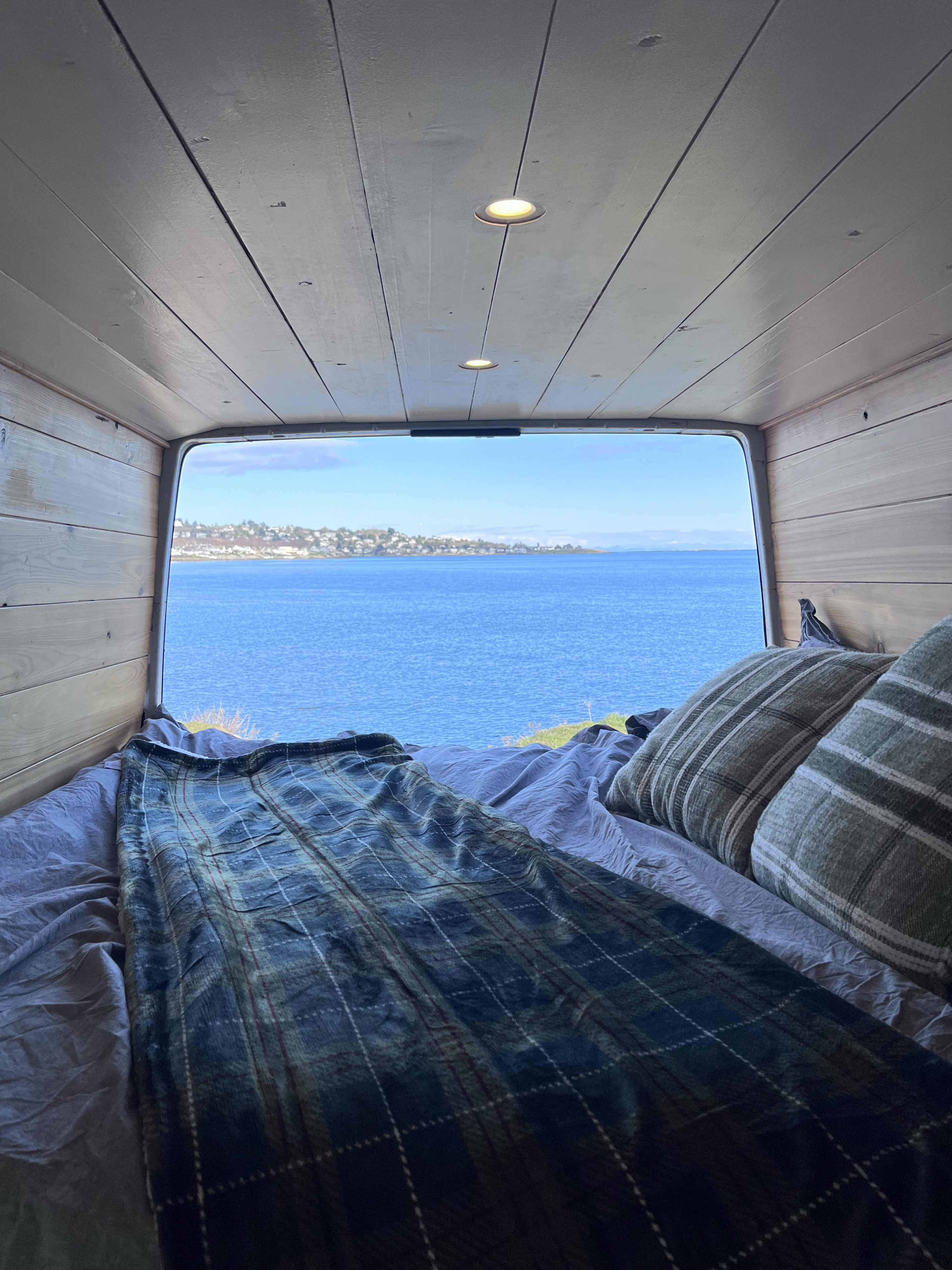 Wake up to this view! Inside a cozy RV rental: bed, plaid blanket, and an incredible blue ocean panorama. #vanlife. Dodge Sprinter Van 2005