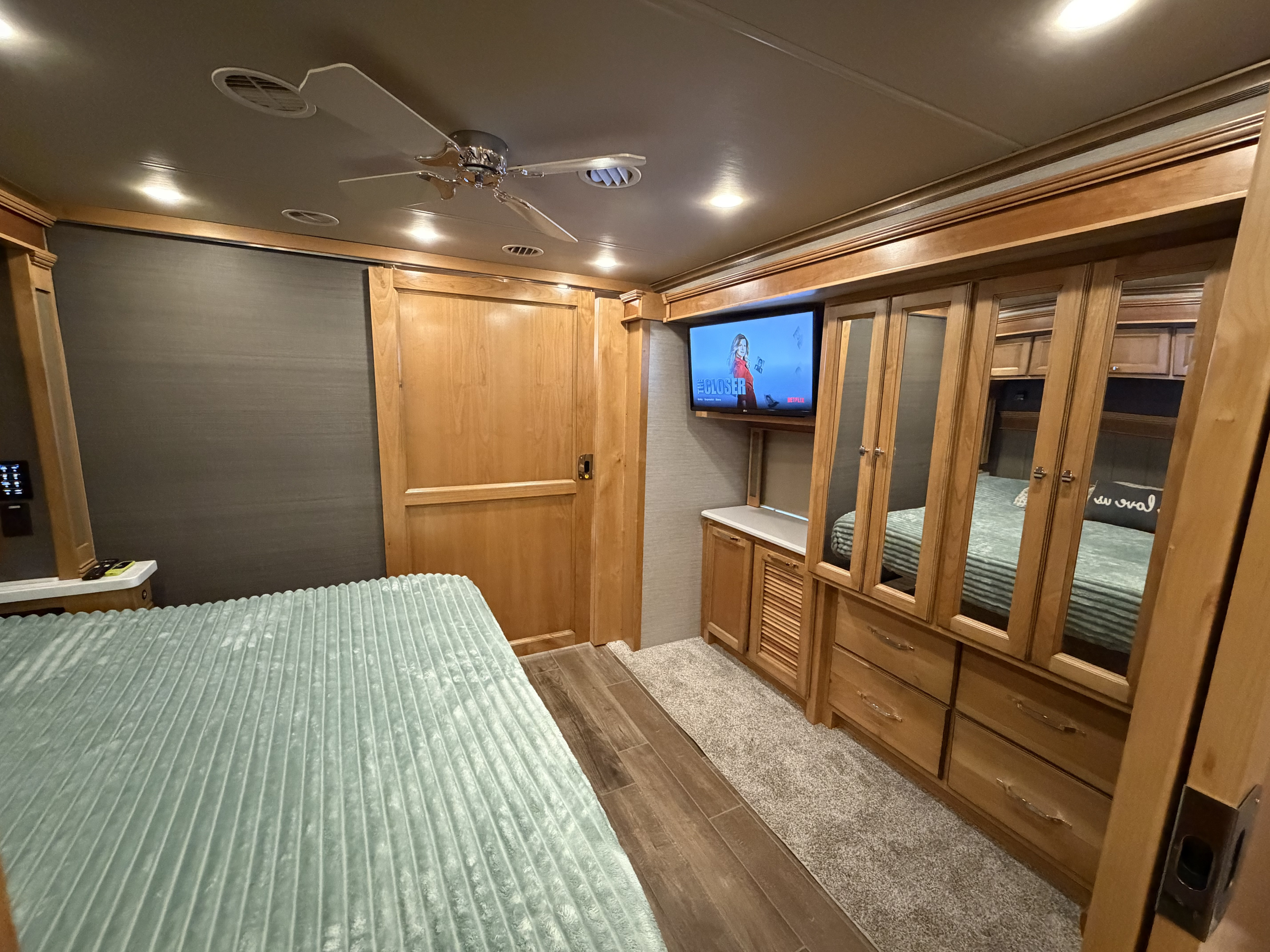 Explore a cozy RV rental bedroom: light wood interior, comfy bed, TV, ceiling fan, and mirrored storage cabinets.. Allegro Allegro Red 360 2022