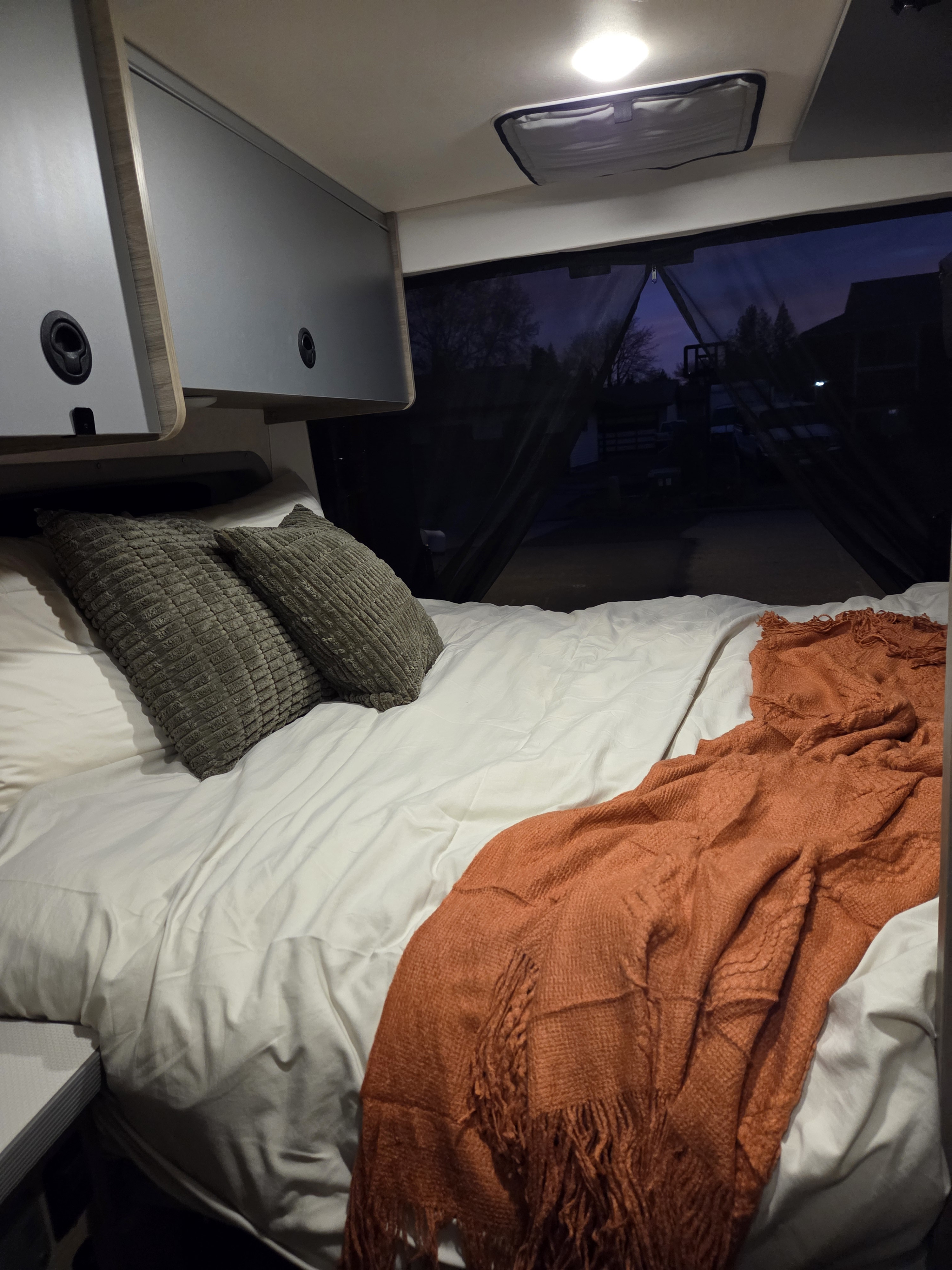 Cozy RV rental bed with textured gray pillows and an orange throw blanket. Perfect for a comfortable night.. Winnebago Solis 2022
