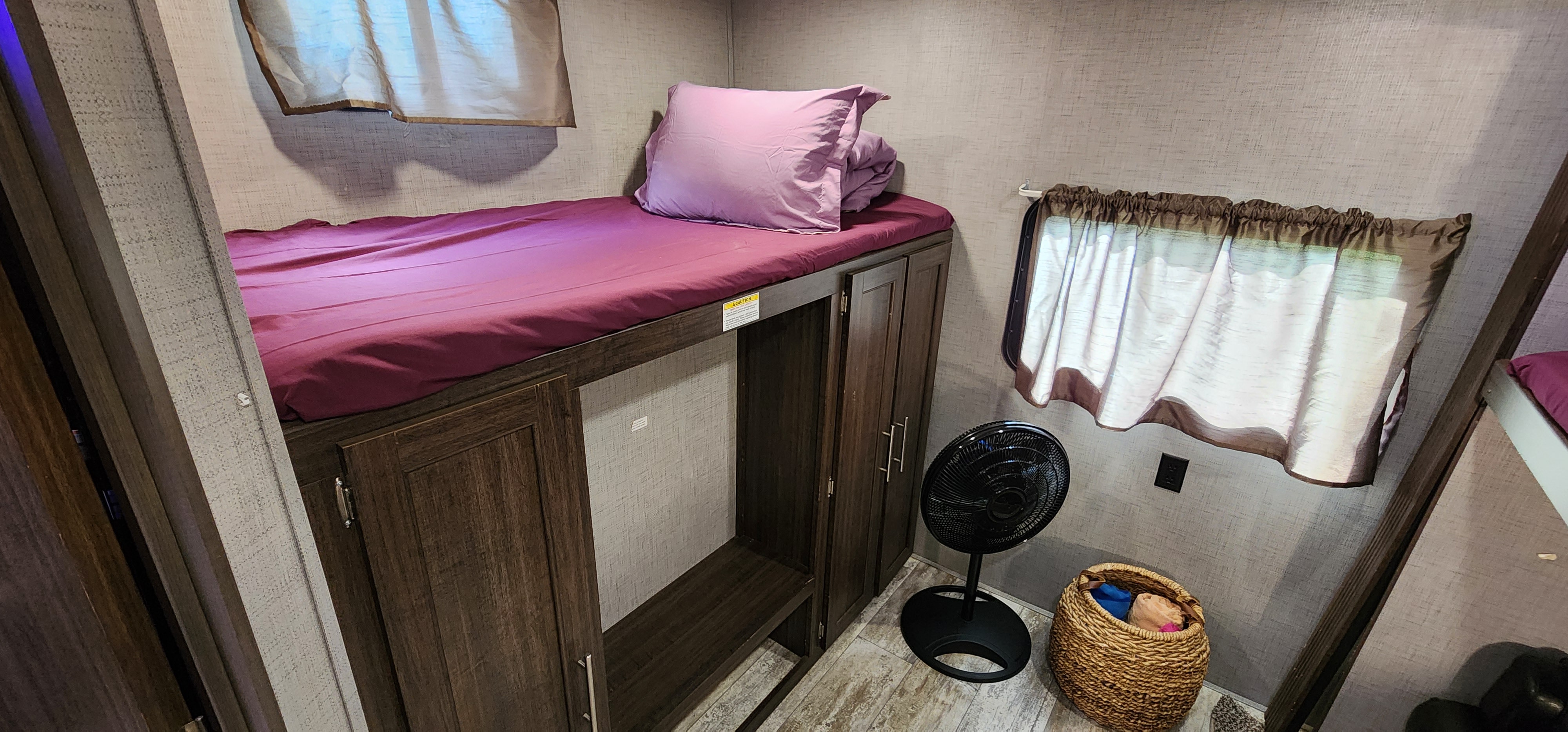 RV rental bunk bed interior with storage, a standing fan, and a woven basket. A compact, functional living space.. Crossroads RV Zinger 2019