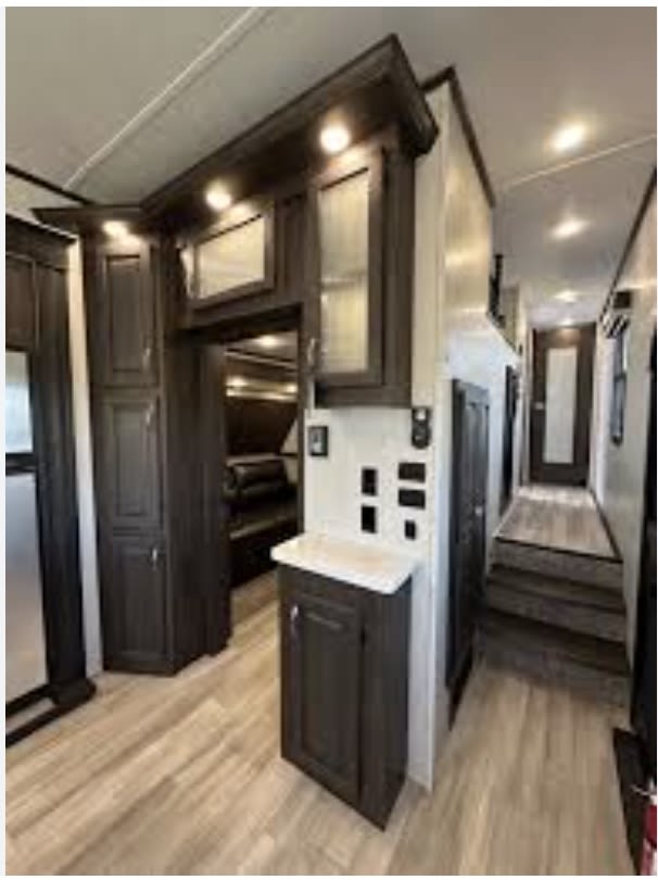 Spacious and modern RV rental interior featuring dark wood cabinets, light floors, a hallway, and bunk beds, perfect for travel.. Coachmen Brookstone 2021