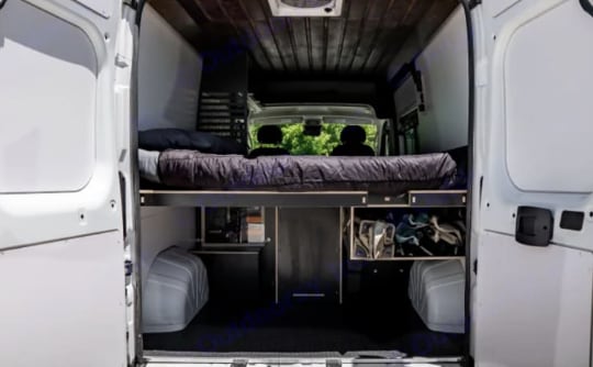 This RV rental offers a cleverly designed camper van interior with a raised bed, under-bed storage, and open rear doors.. Ram Promaster 1500 High-Roof 2021