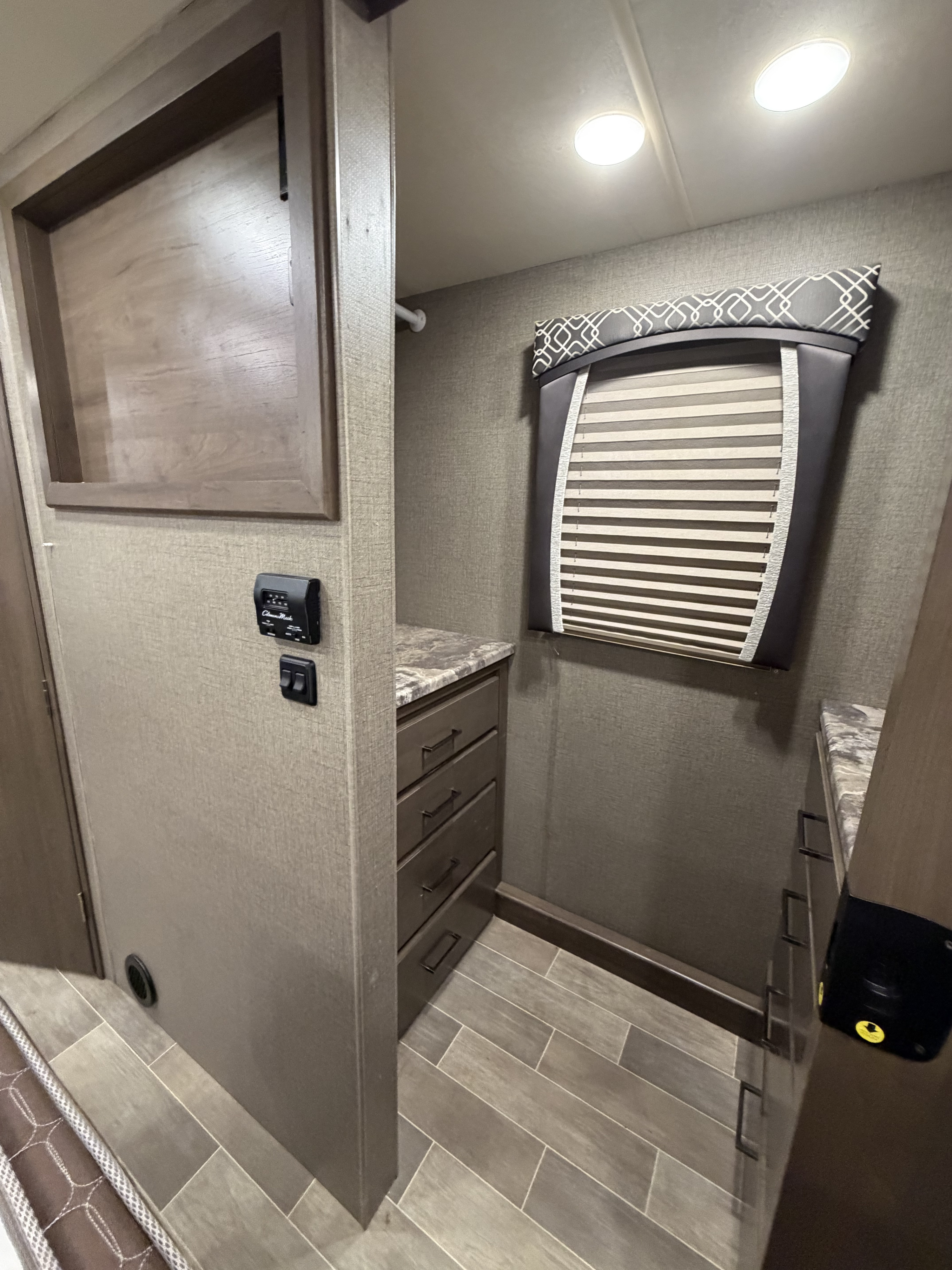 Inside an RV rental: a built-in closet with drawers, window blinds, thermostat, and overhead lighting.. Thor Chateau 2021