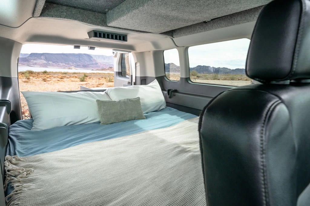 Inside this RV rental, a comfy camper van bed awaits, offering stunning desert and lake views from the rear.. Ford Transit 2023