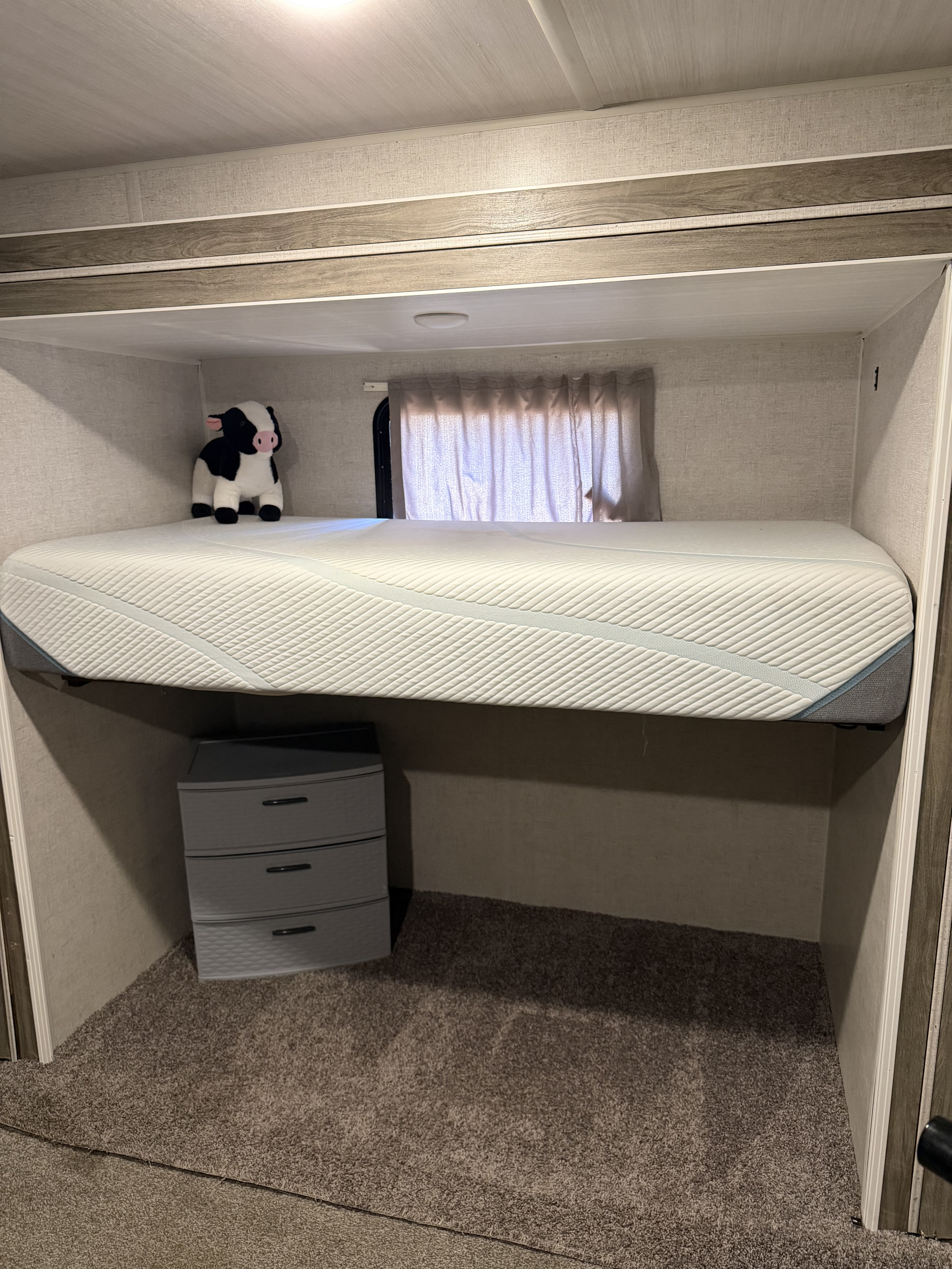Cozy RV rental interior: bunk bed with mattress, stuffed cow, storage dresser, and window with curtains.. Forest River Wildwood 2022