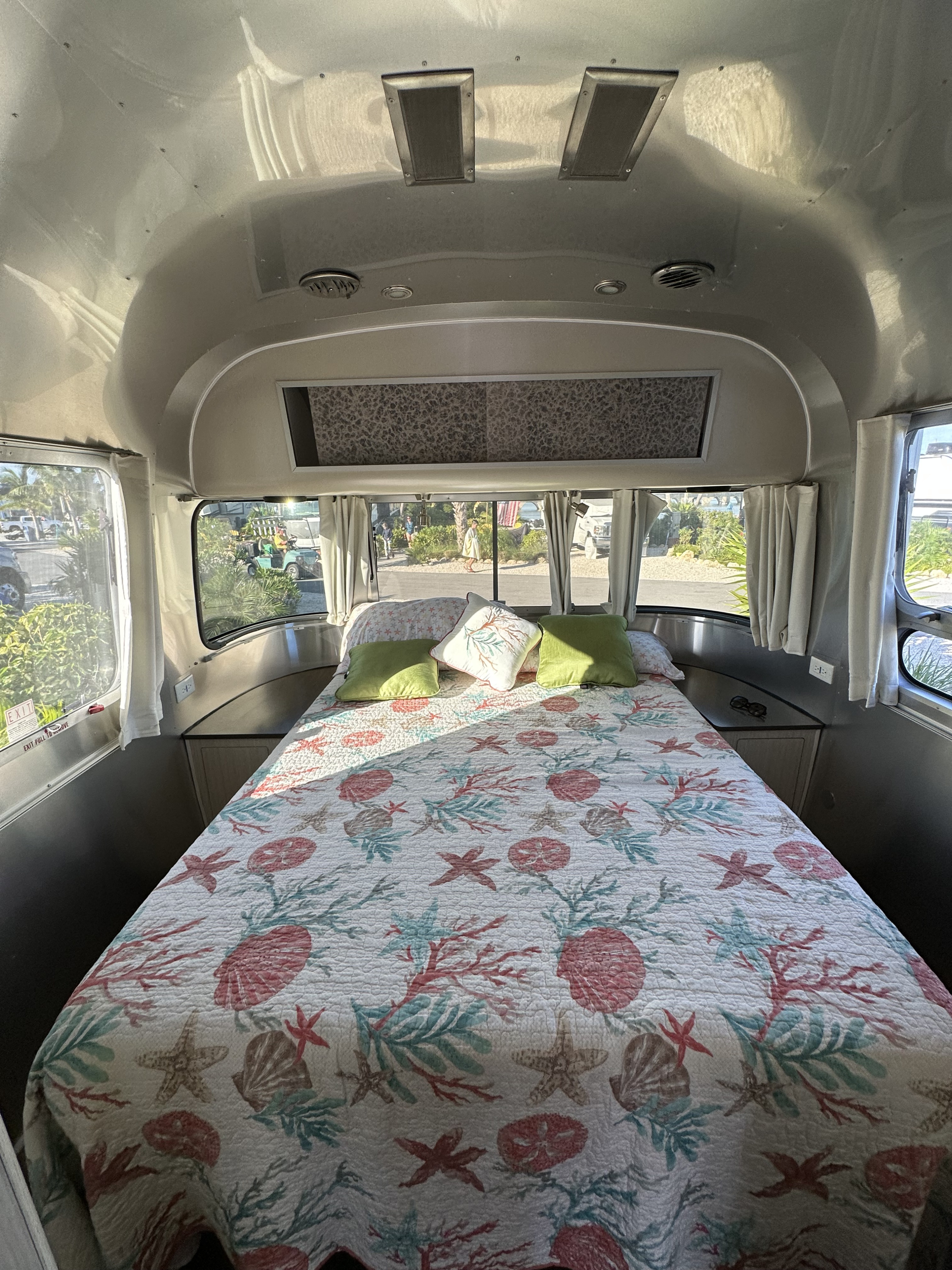 Cozy RV rental bedroom featuring a bed with a vibrant seashell quilt, surrounded by large windows offering natural light.. Airstream International 2020