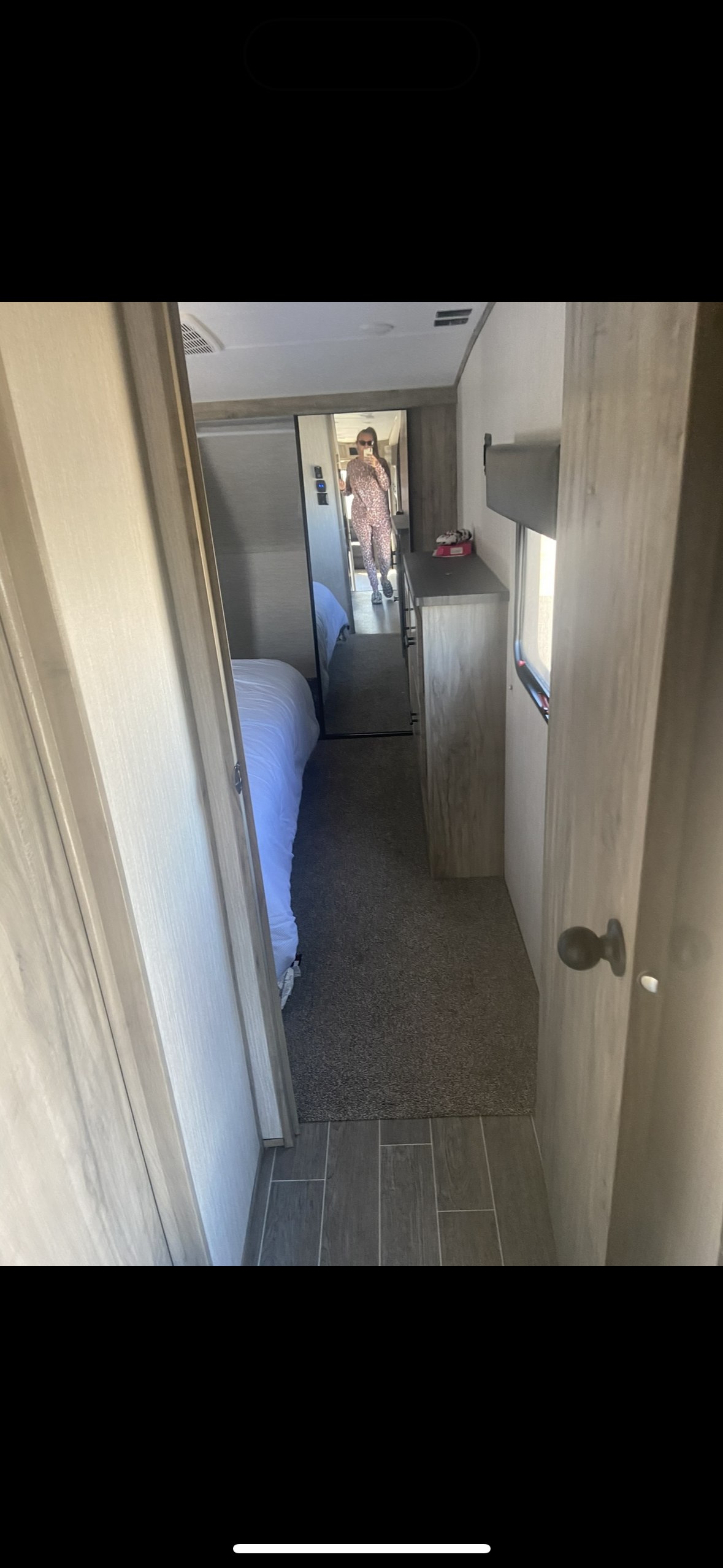 RV rental bedroom view. A mirror reflects a person in a patterned outfit. Shows a bed, dresser, and tiled/carpeted floor.. Forest River Cherokee Arctic Wolf 2020